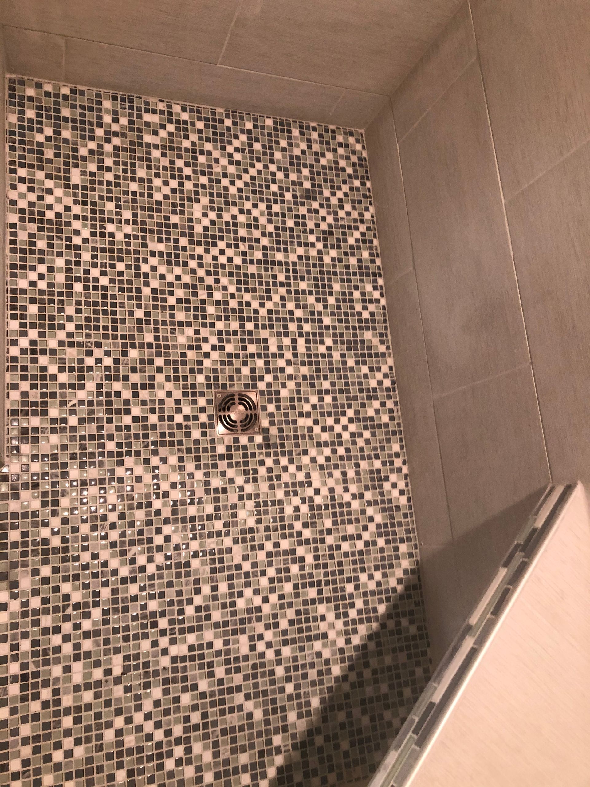 Small mosaic-tiled shower corner with a drain and a slanted white panel on the right