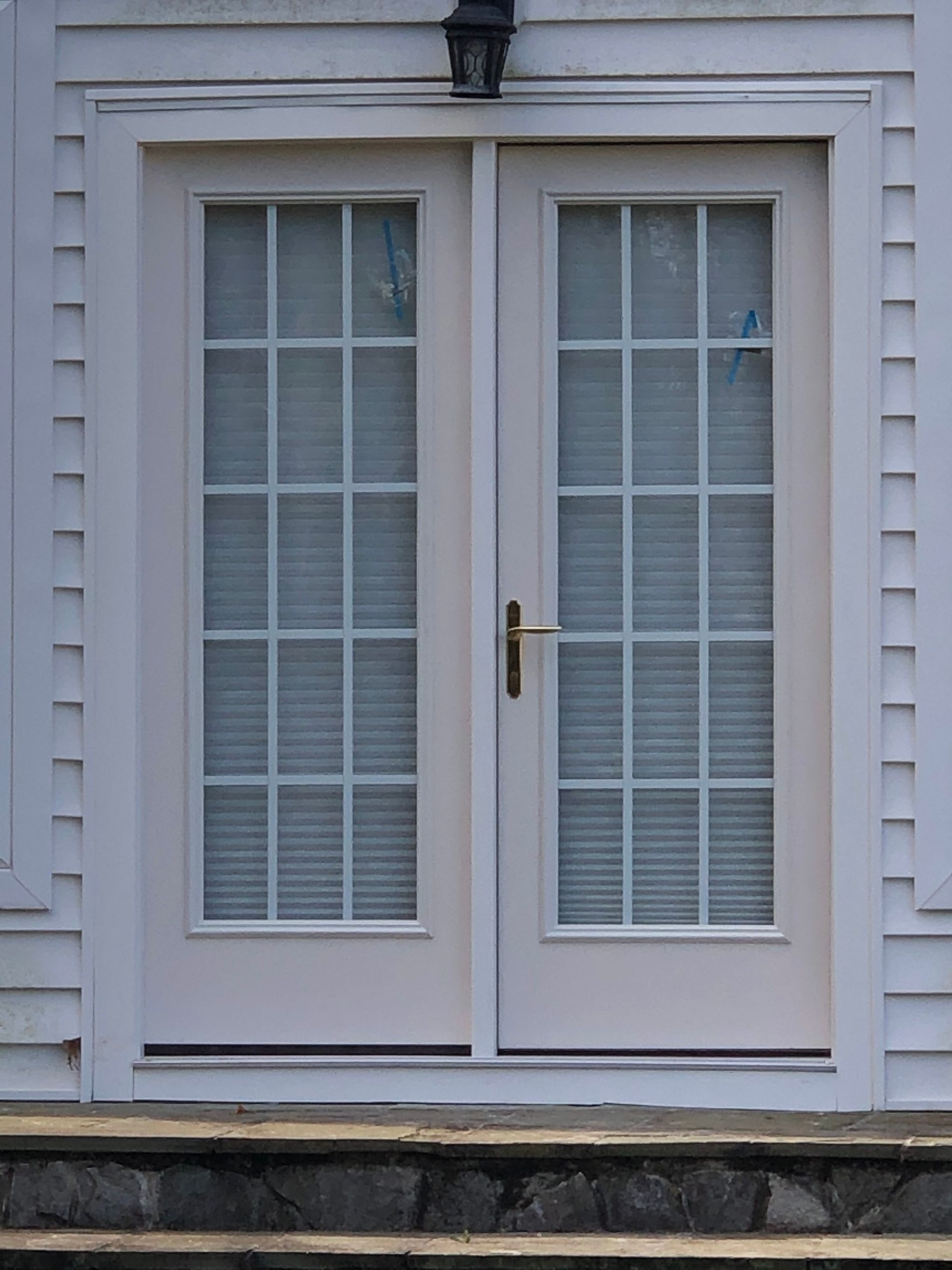 White French doors with glass panes and blinds beneath a wall-mounted light.