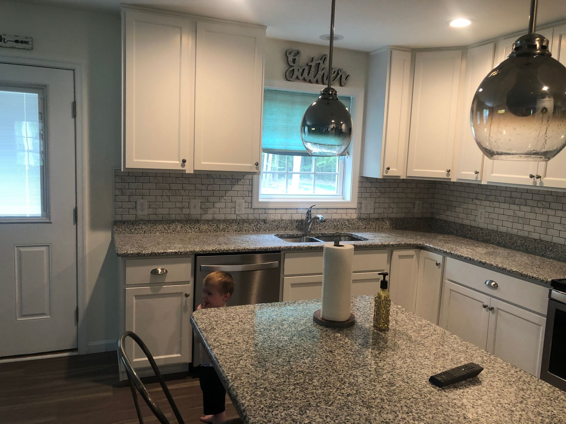 Modern white kitchen with black pendant lights, granite island, and tiled backsplash