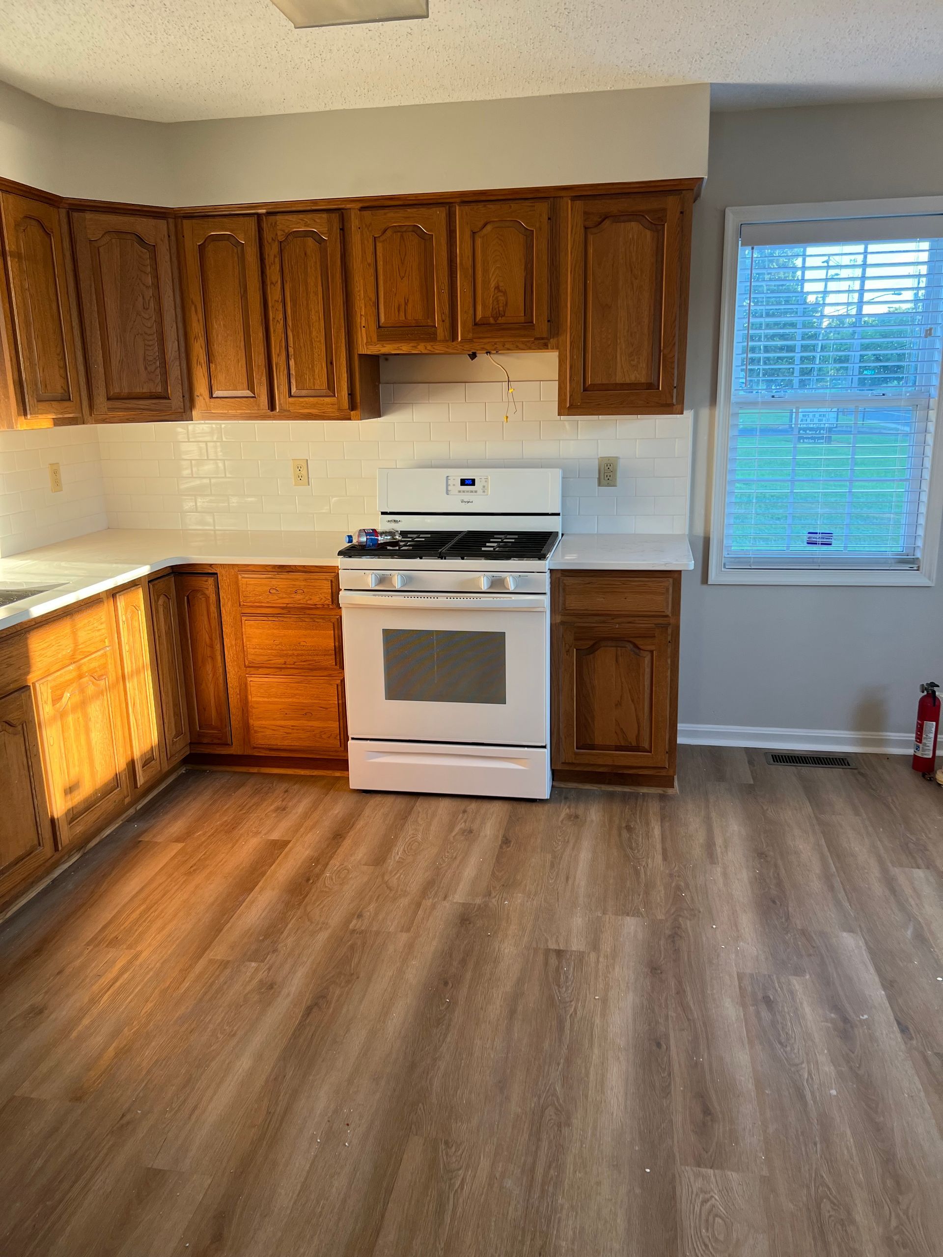Empty kitchen with wood cabinets, white stove, and large window on wood-look flooring