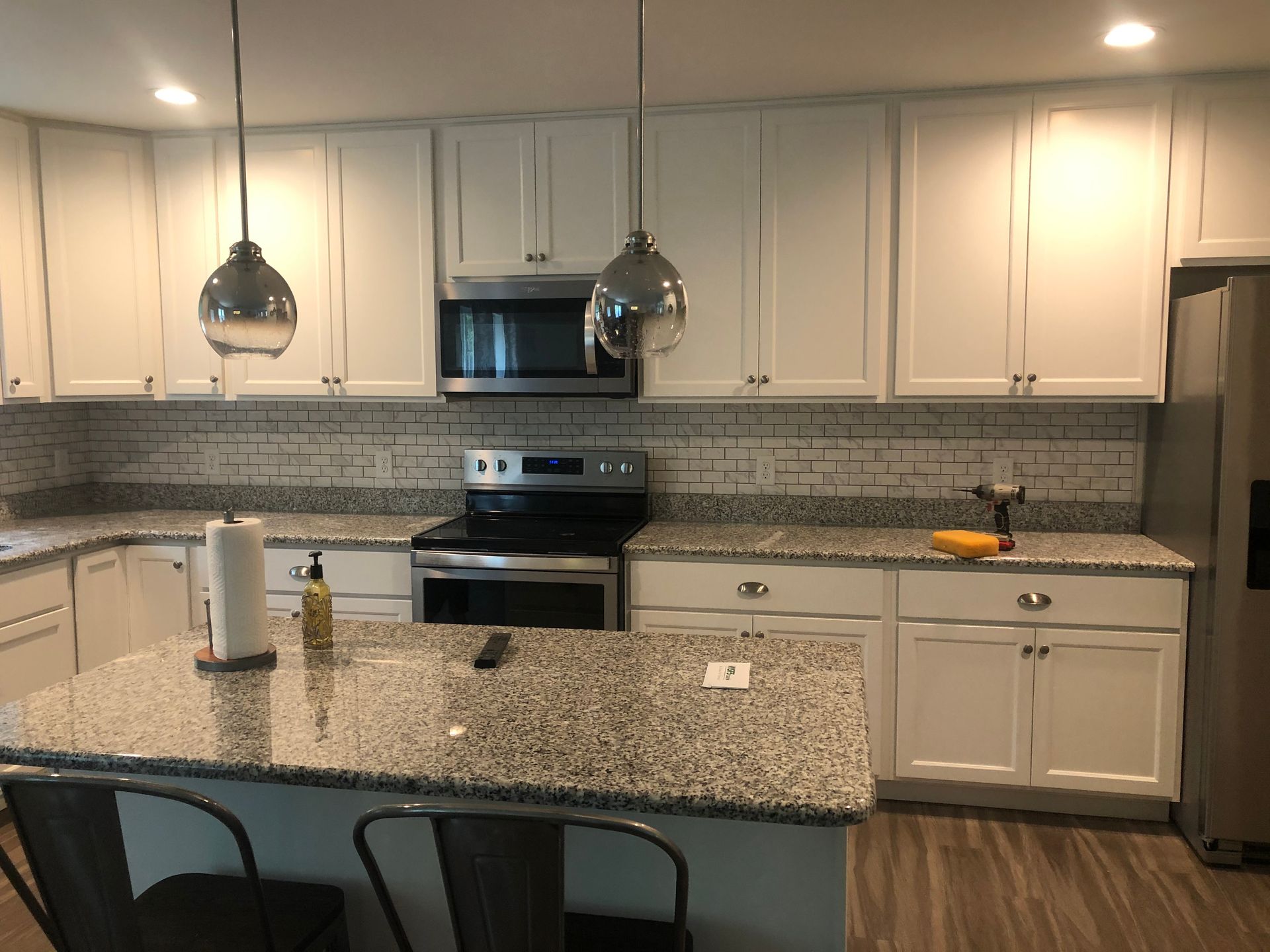 Bright modern kitchen with white cabinets, granite island, stainless appliances, and pendant lights.