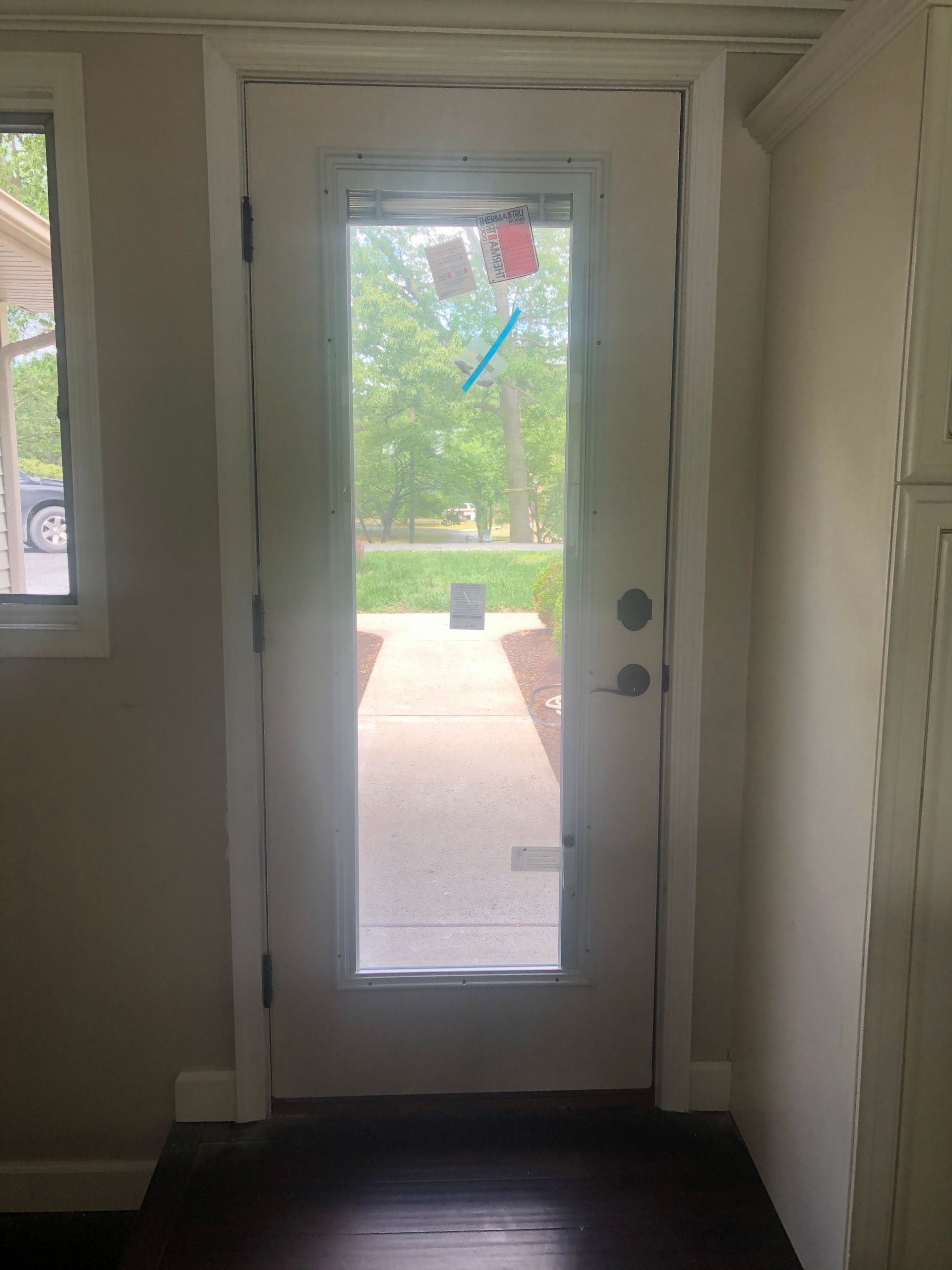 Interior view of a front door with a narrow glass panel opening to a green yard outside.