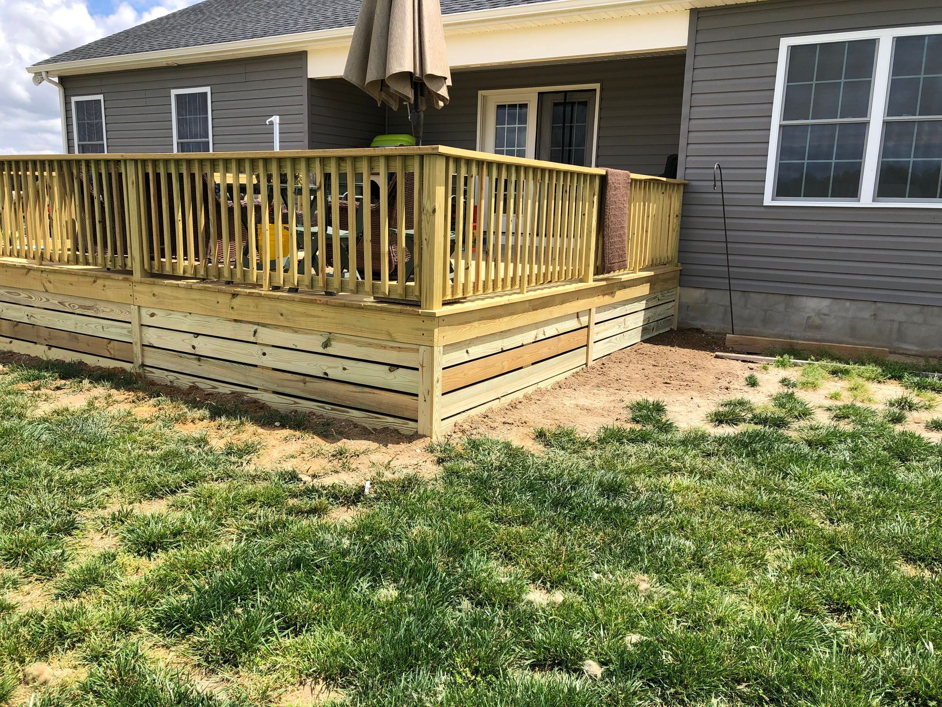 Wooden backyard deck with railing attached to a house, overlooking a grassy yard