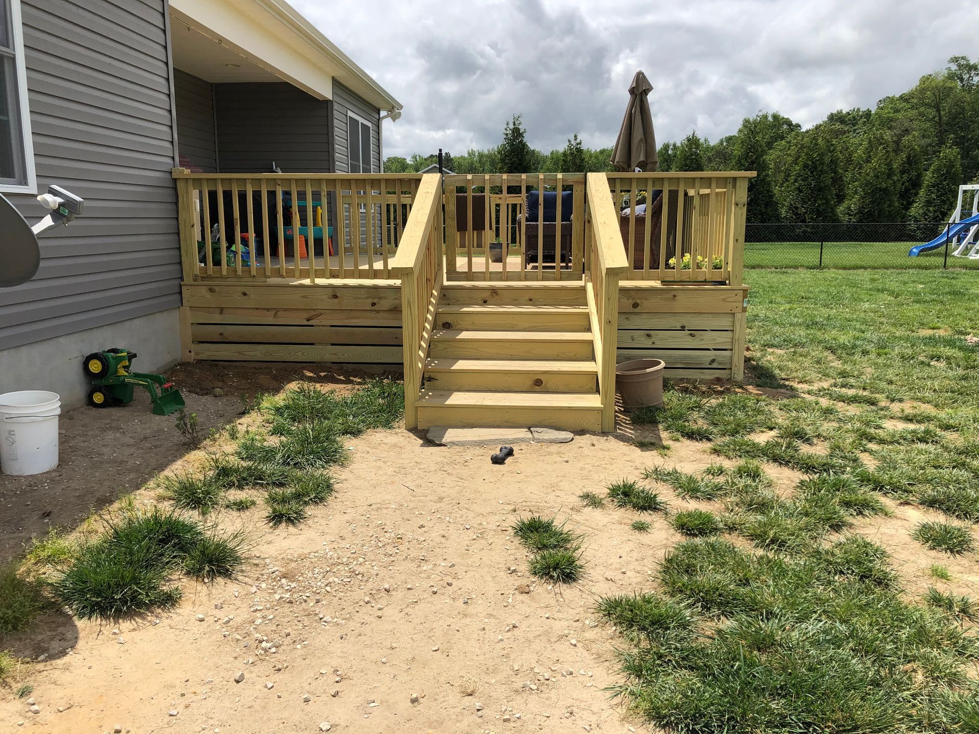 Wooden backyard deck with steps beside a house, surrounded by a grassy yard and overcast sky