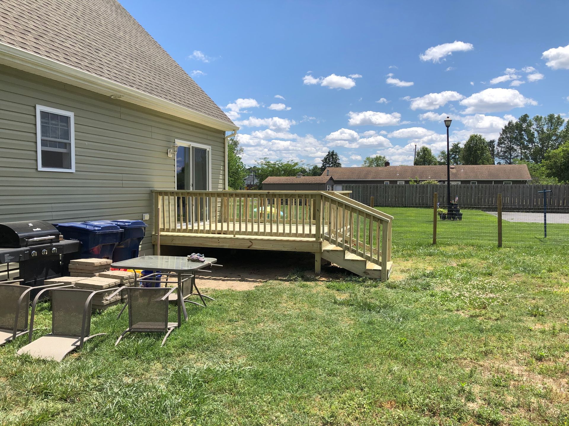Backyard with a small wooden deck on a house, patio chairs, and a grassy yard under a blue sky