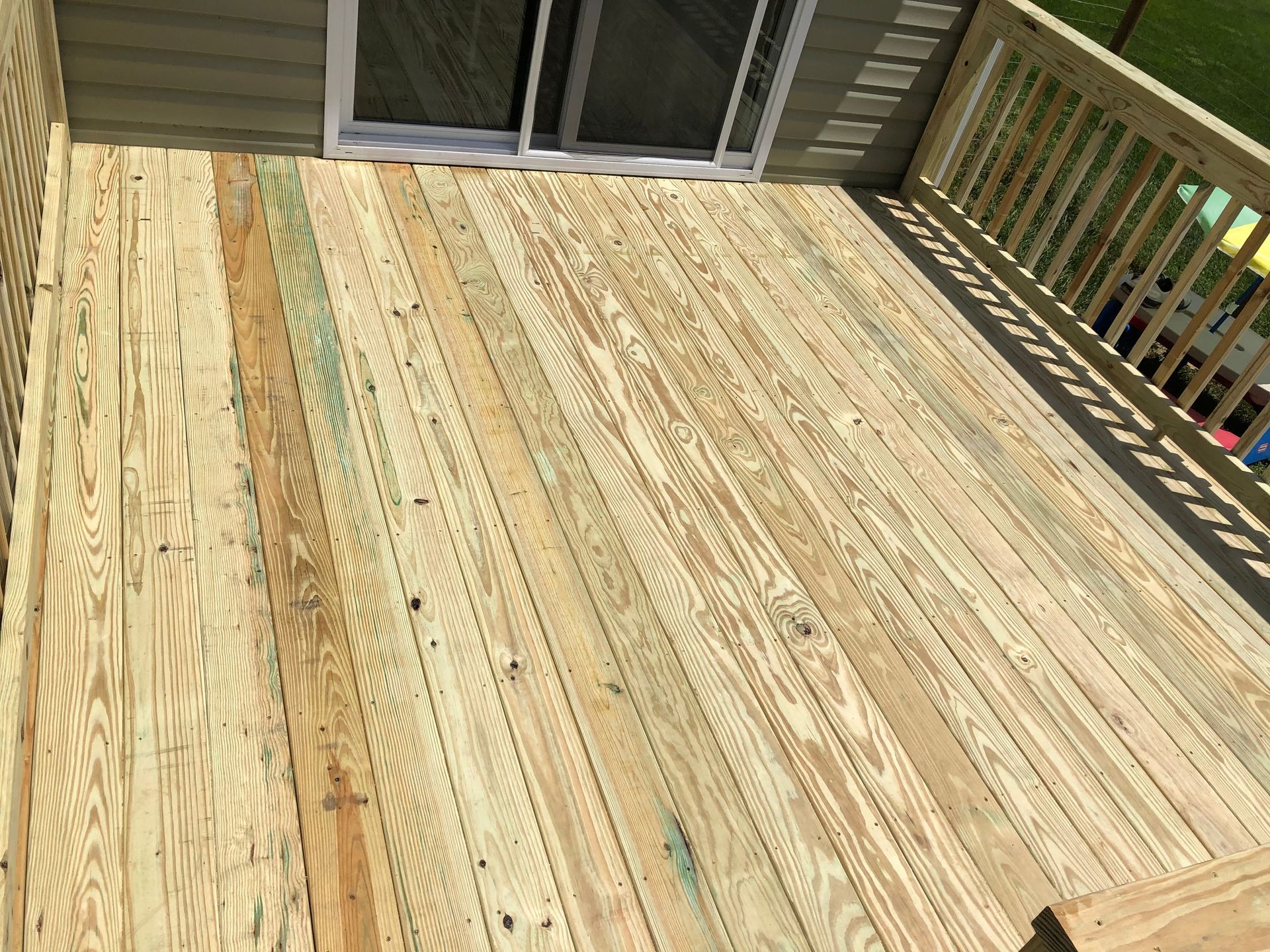 Empty wooden deck with sliding glass doors and railing in sunlight