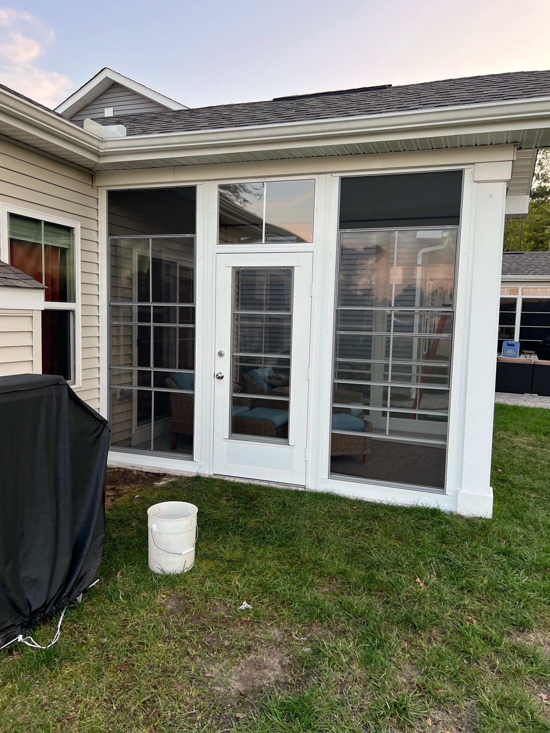 White-framed glass sunroom addition on the back of a house with grass in front