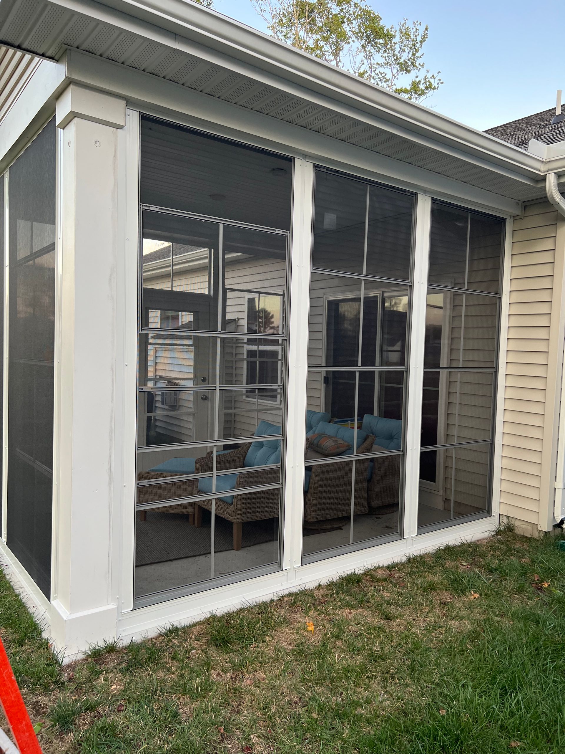 Sunroom with large screened windows and gray trim beside a house, with grass in front
