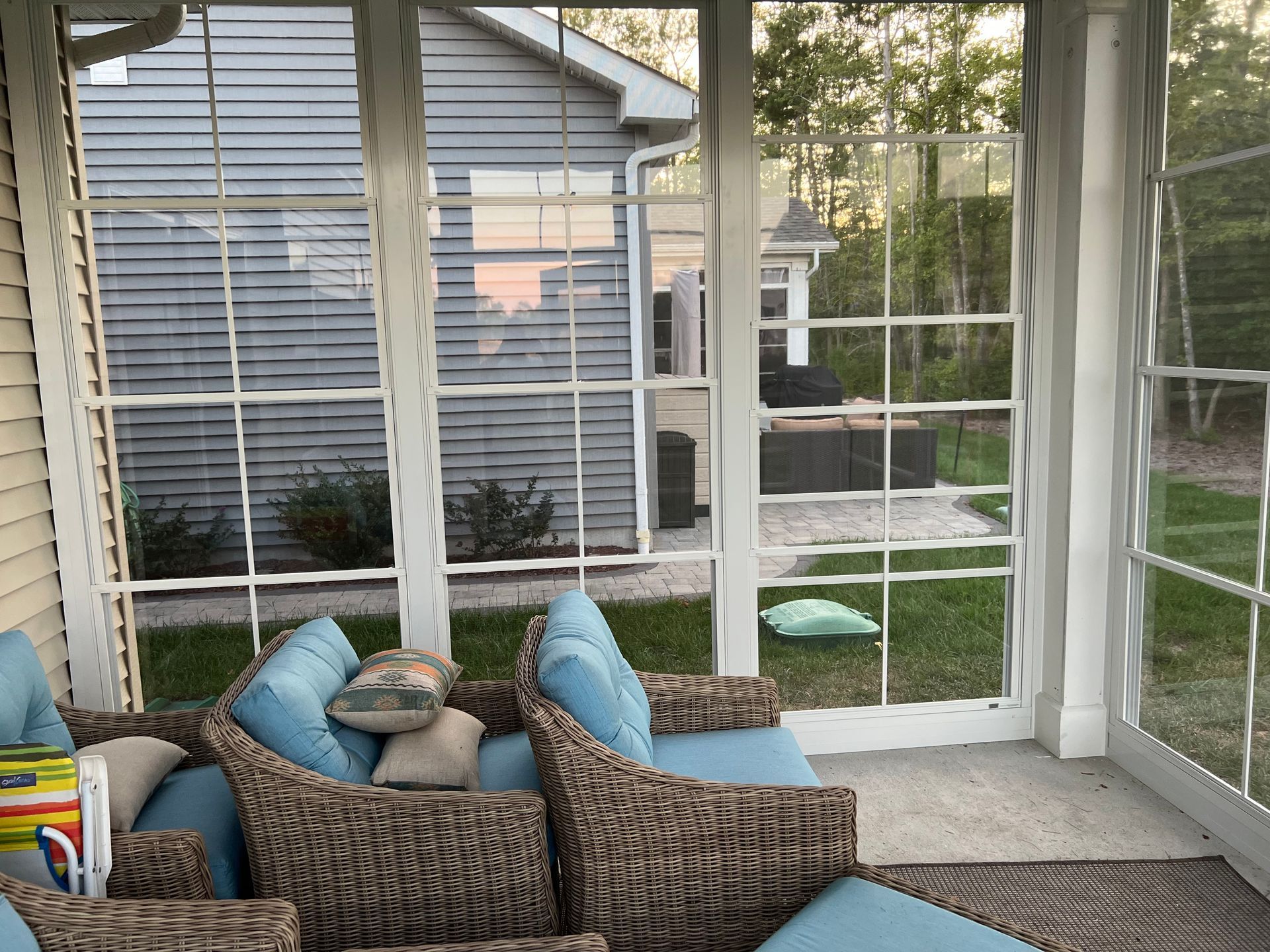 Screened porch with wicker chairs and blue pillows overlooking a backyard and neighboring houses