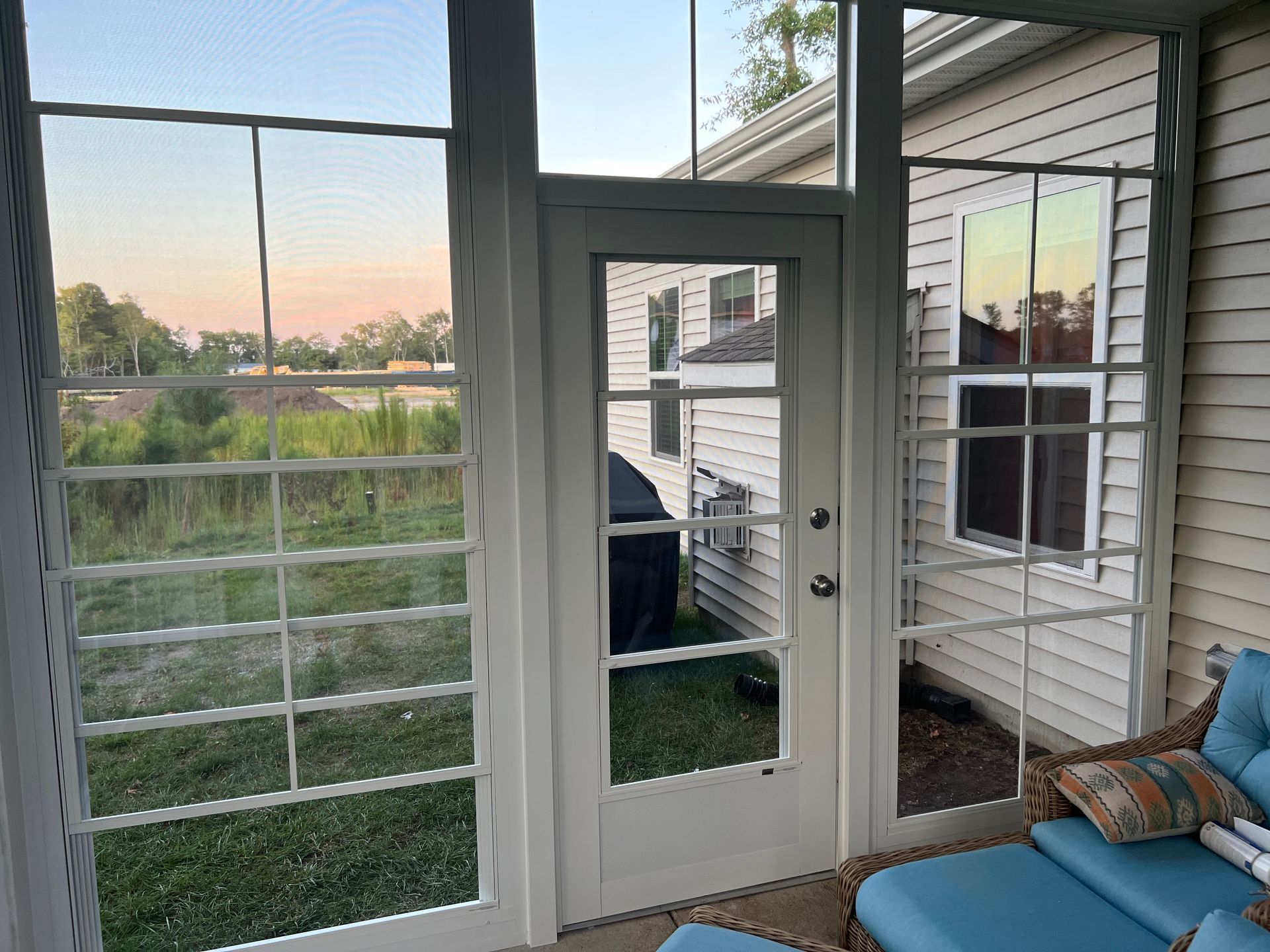 Sunroom with white-framed glass door, large windows, and a couch overlooking a grassy yard at sunset