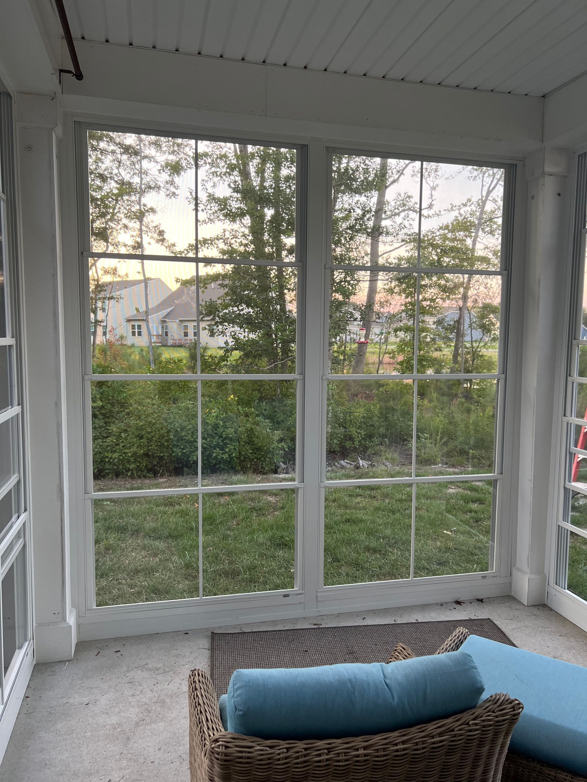 Sunroom with large windows, patterned rug, and blue cushion overlooking a grassy backyard at sunset