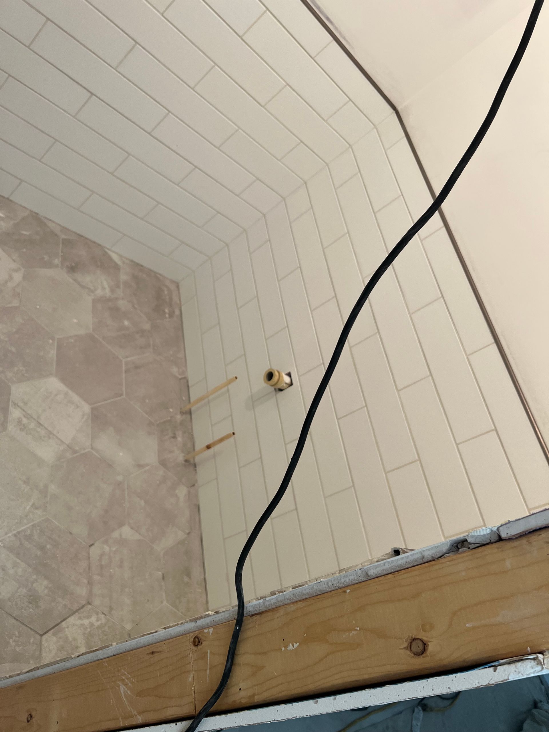 Curved white tiled wall with a black cable hanging down and a wooden beam at the bottom