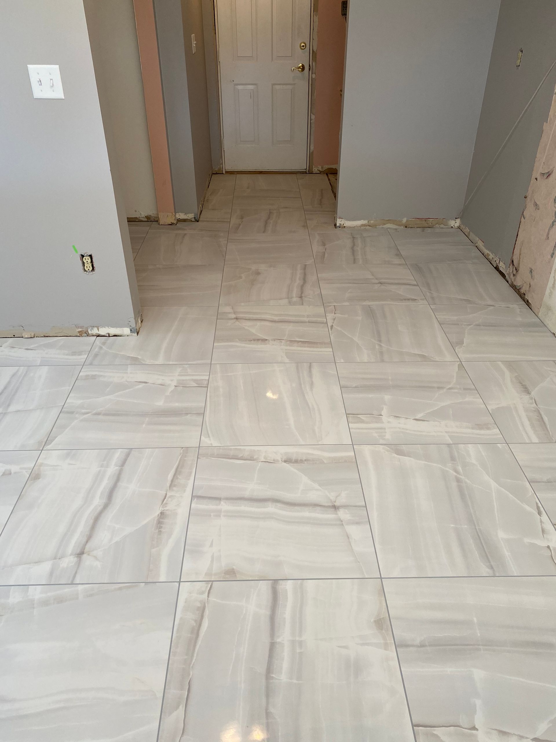 Empty hallway with newly tiled white floor and unfinished gray walls, viewed toward a closed white door