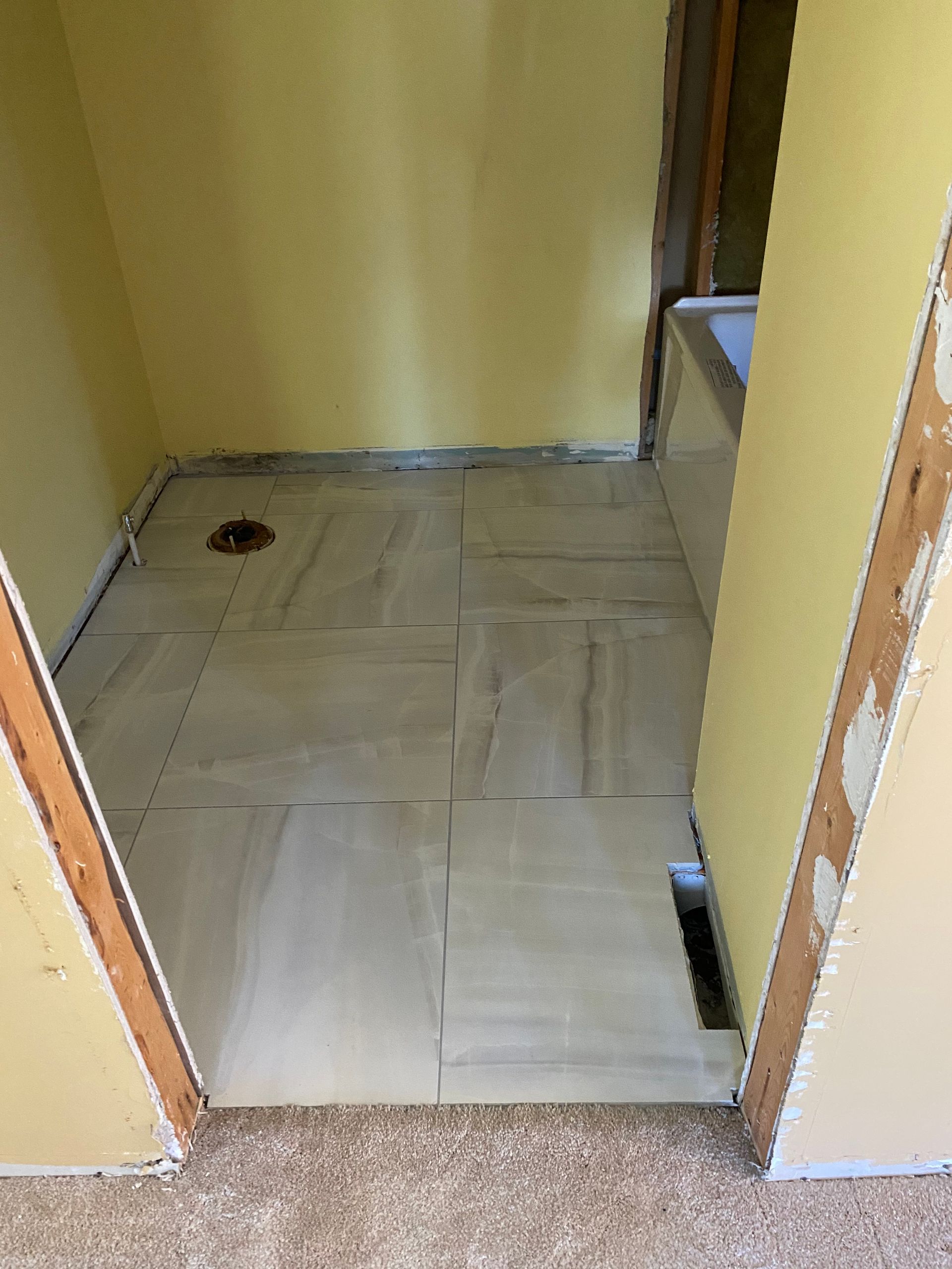Narrow hallway with unfinished tiled floor and exposed walls, leading to a doorway.