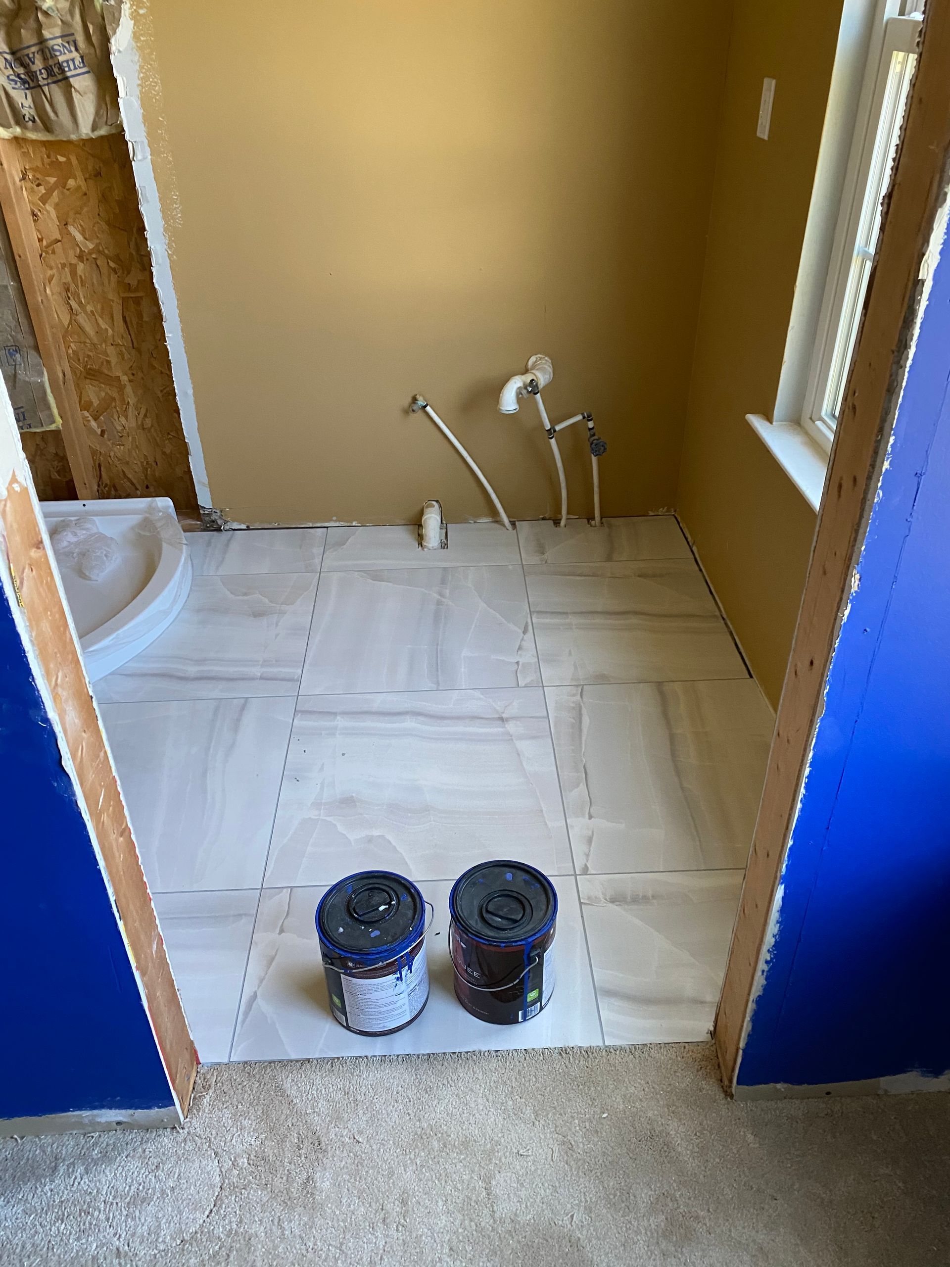 Partially tiled bathroom under renovation, with paint cans and plumbing fixtures visible.