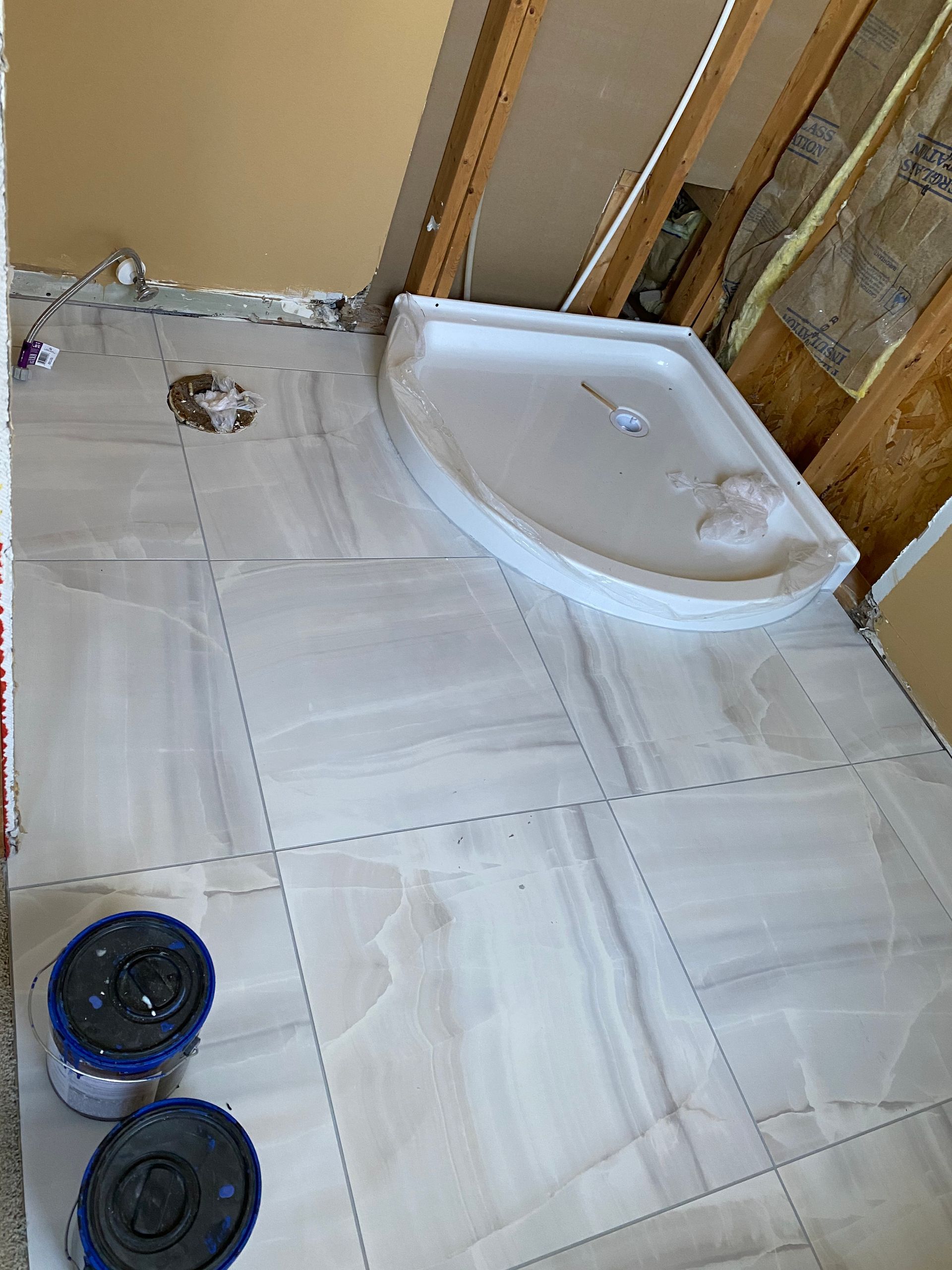 Small bathroom under renovation with white floor tiles, a shower base, and two black buckets.