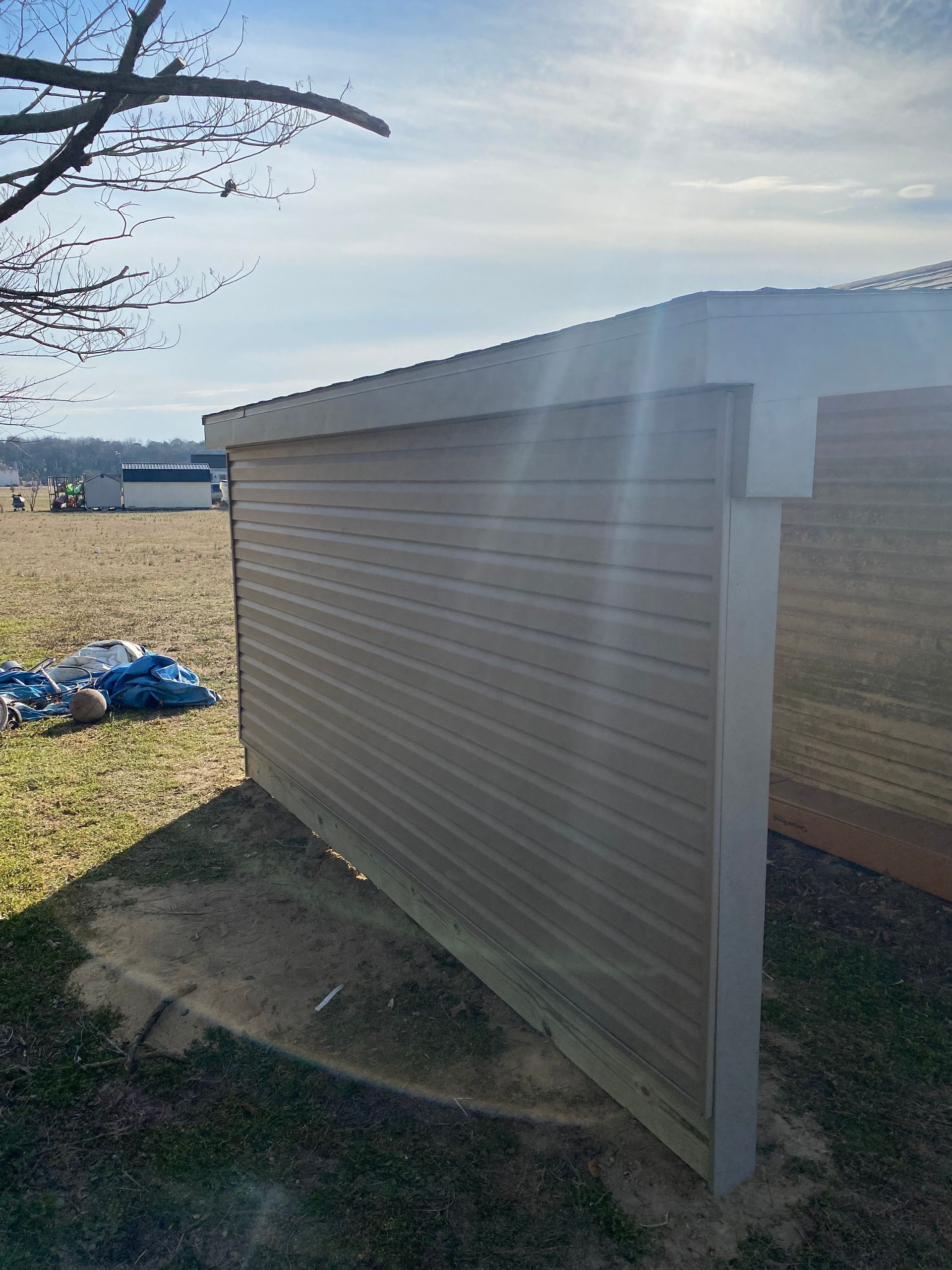 White corrugated metal shed beside a grassy field under a sunny sky