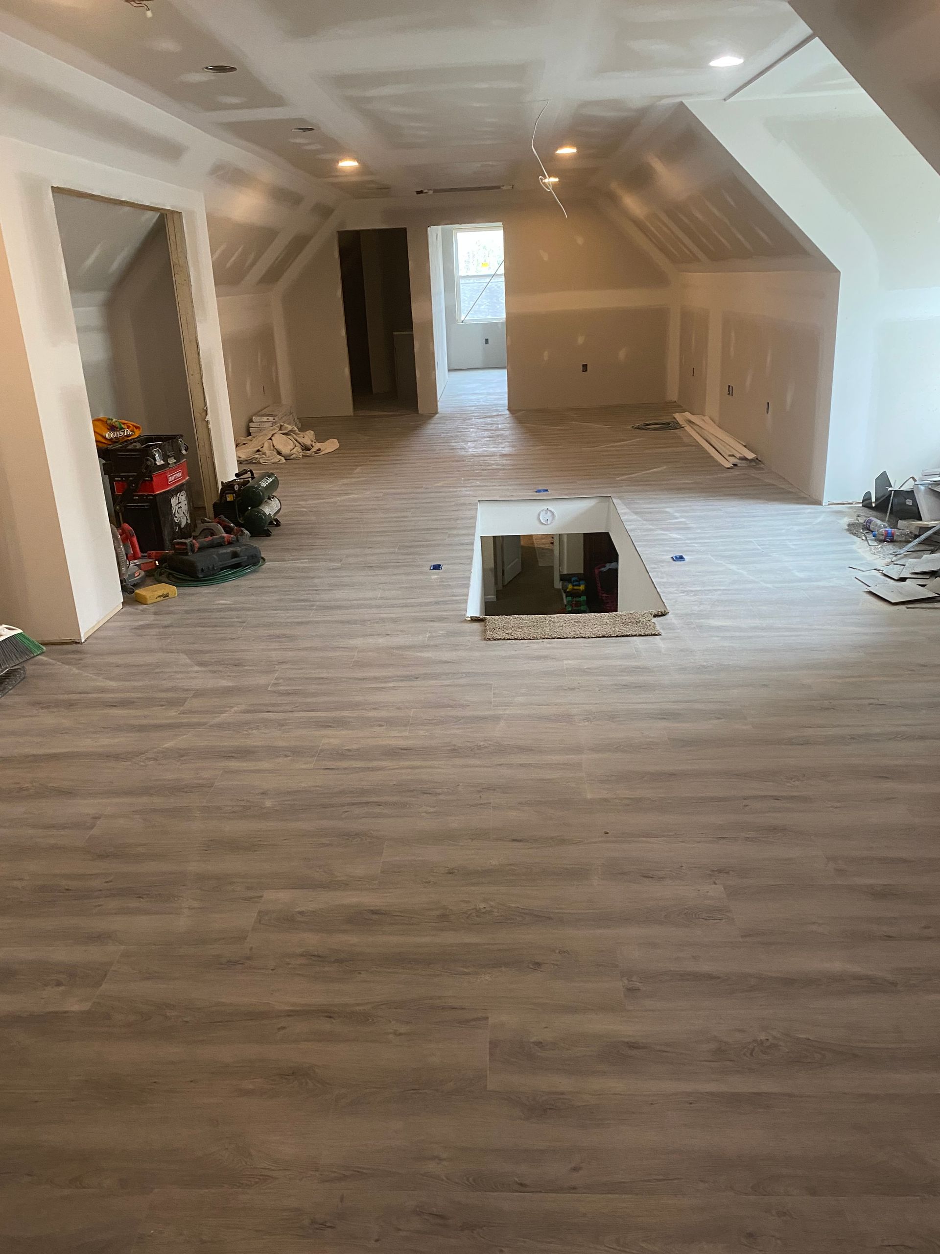 Long room with white walls, gray wood flooring, recessed lights, and a floor opening in the center during renovation