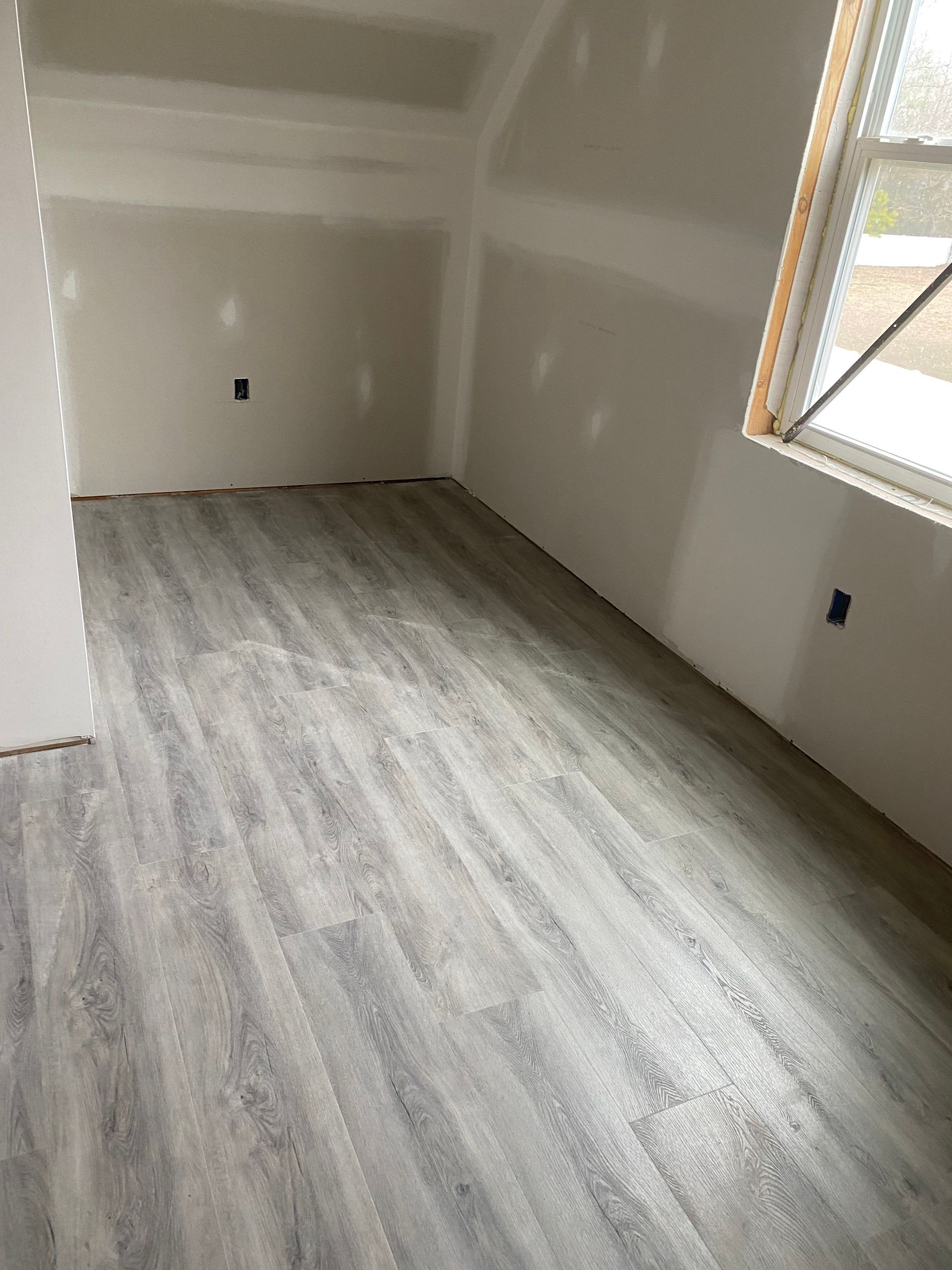 Empty room with gray wood-look flooring, white walls, and a window on the right.