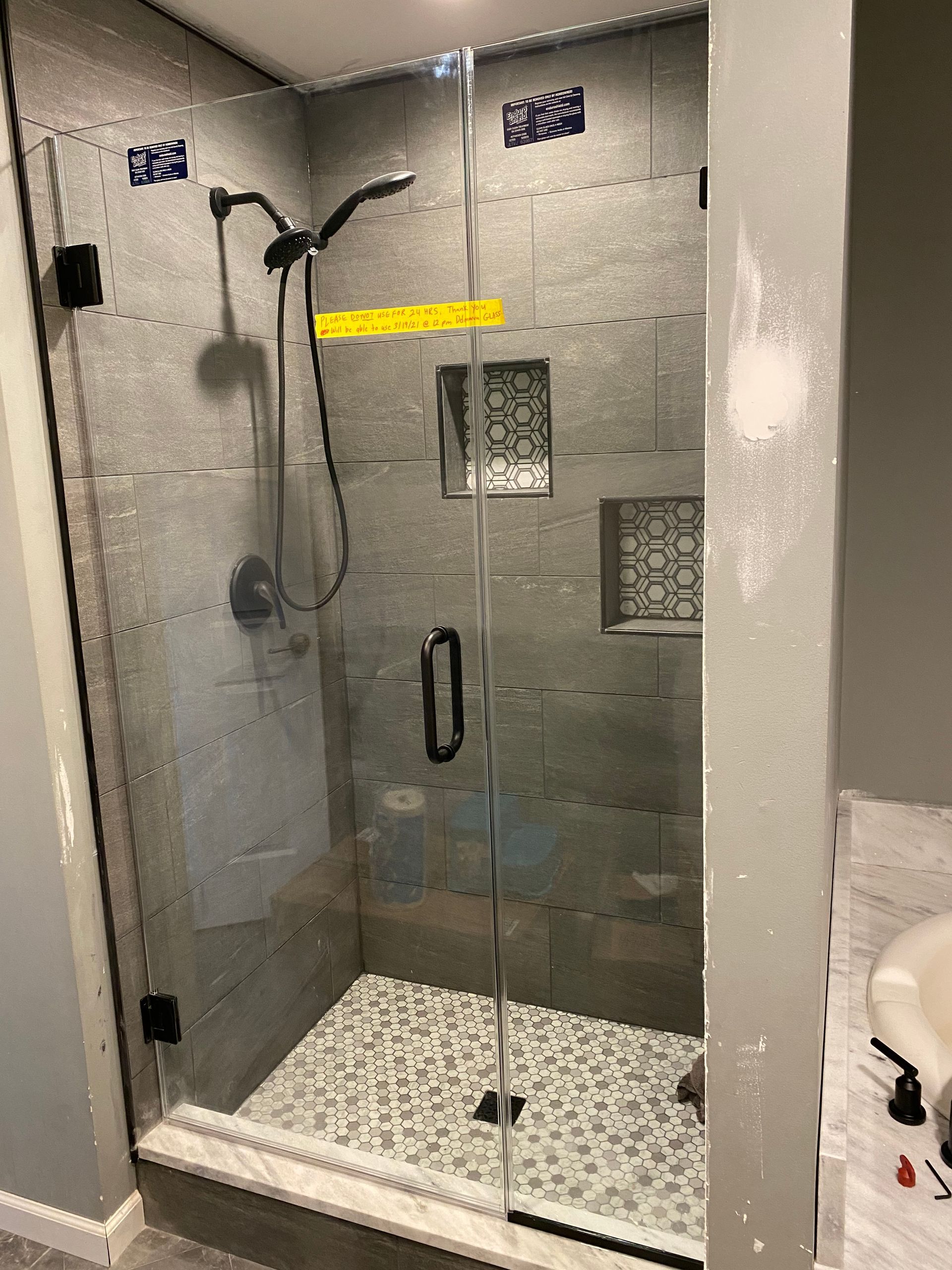 Accessible walk-in shower with grab bar, handheld showerhead, glass door, and pebble shower floor.
