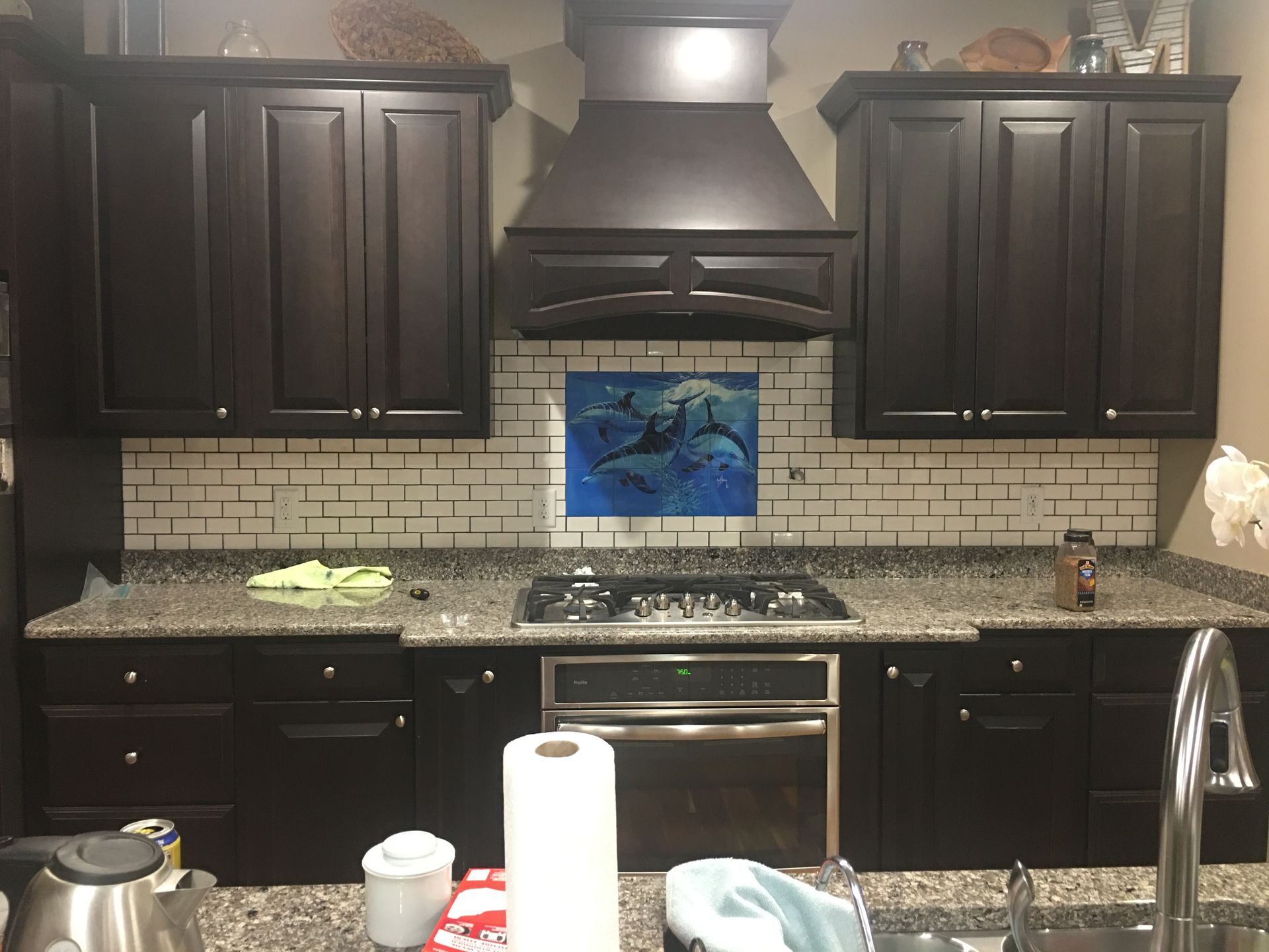 Dark kitchen with black cabinets, granite counters, stainless stove, and a blue wall picture above the backsplash.