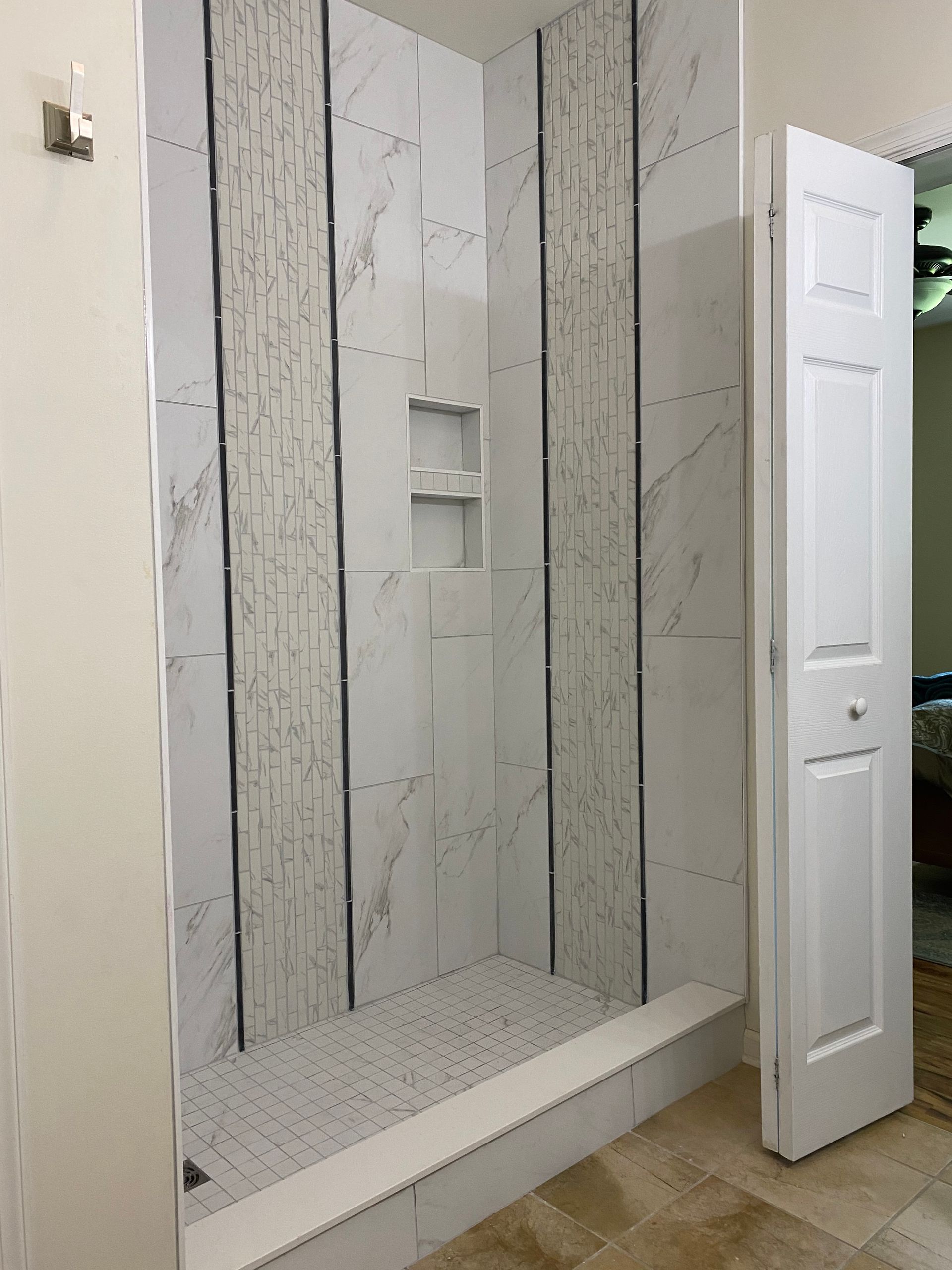 Modern walk-in shower with white tile, gray marble accents, built-in shelves, and a low bench