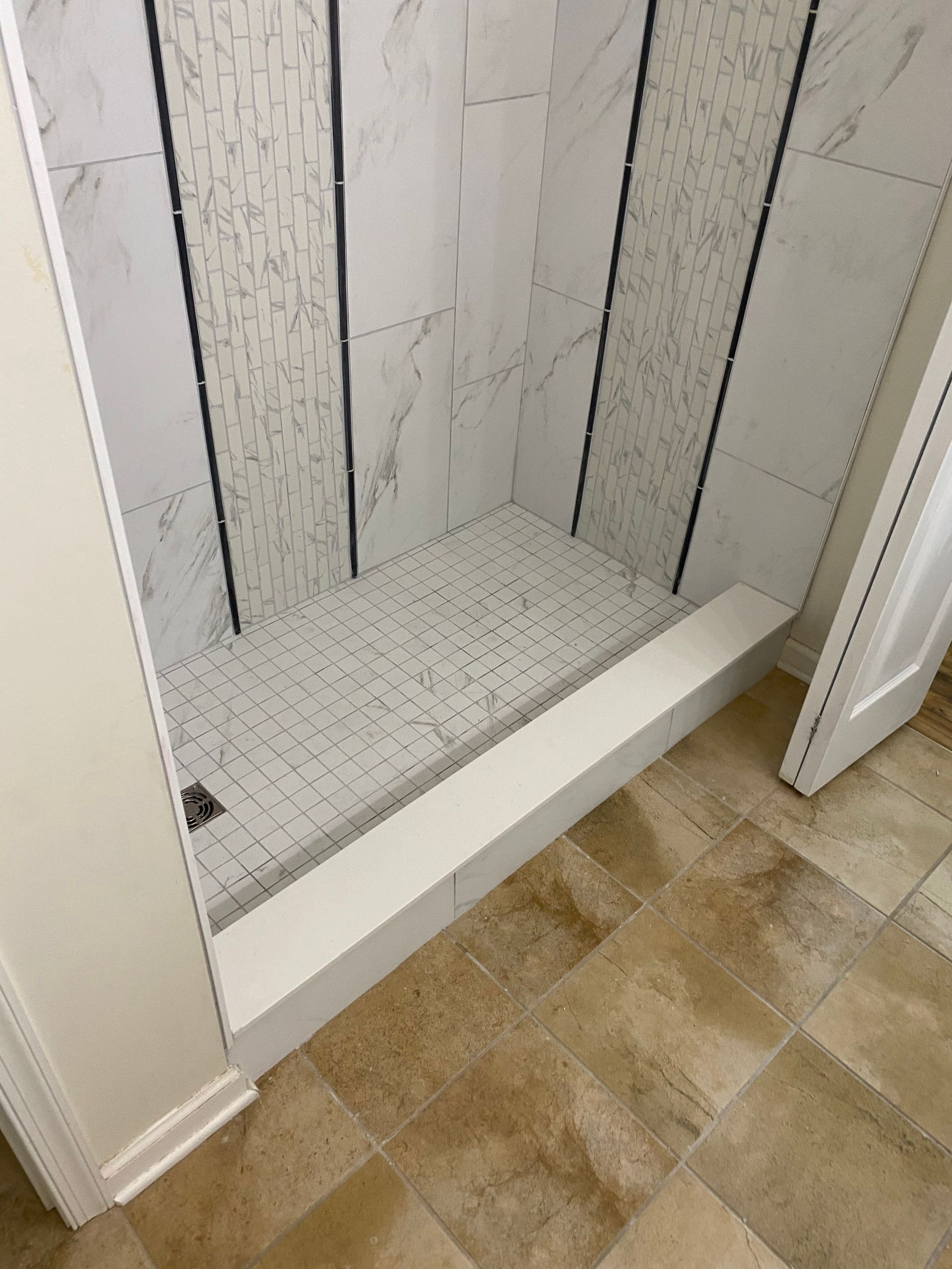 Walk-in shower with white tiled walls and floor beside beige tile flooring