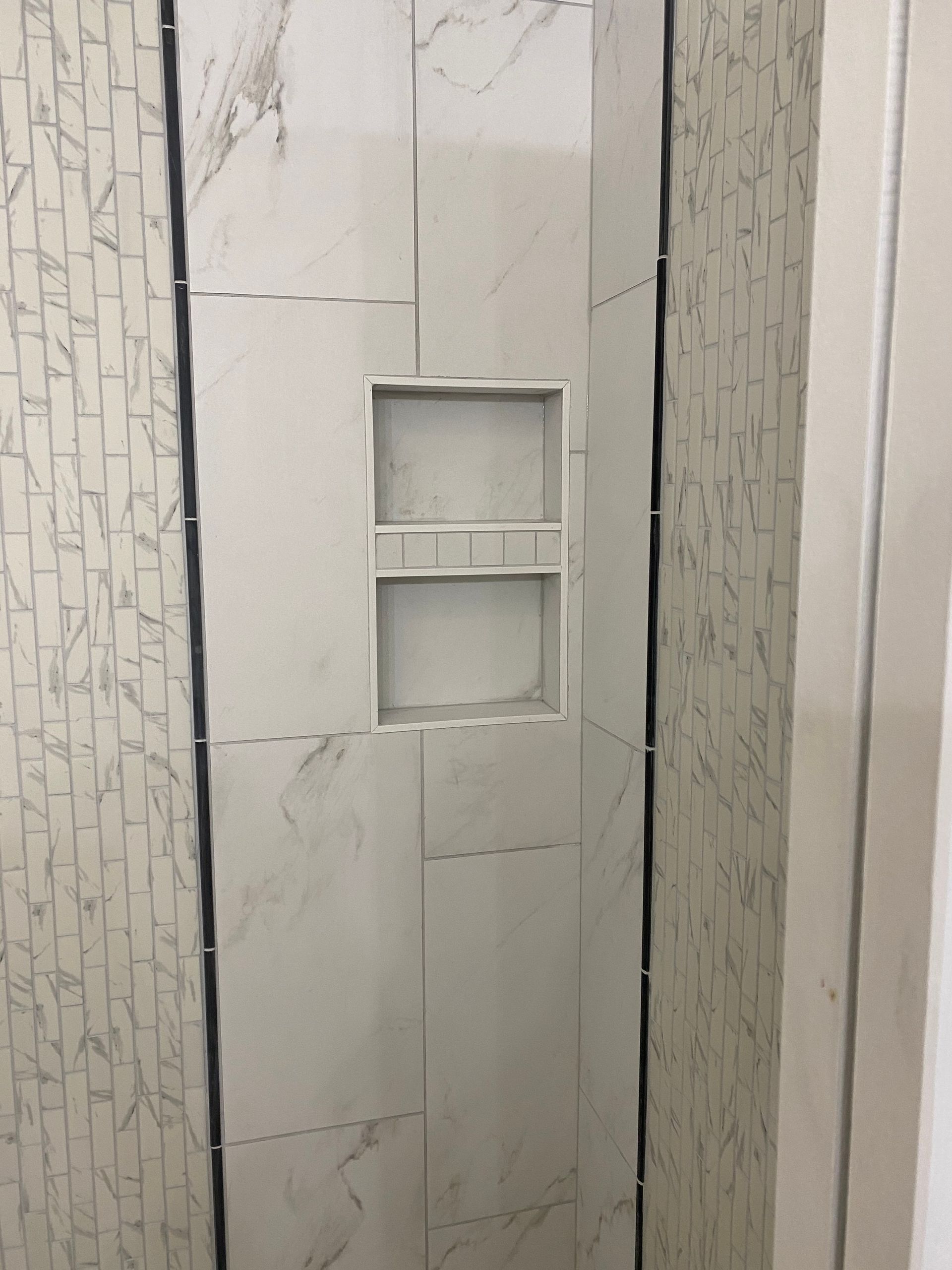 White tiled shower wall with a recessed niche and mosaic accent strips on both sides