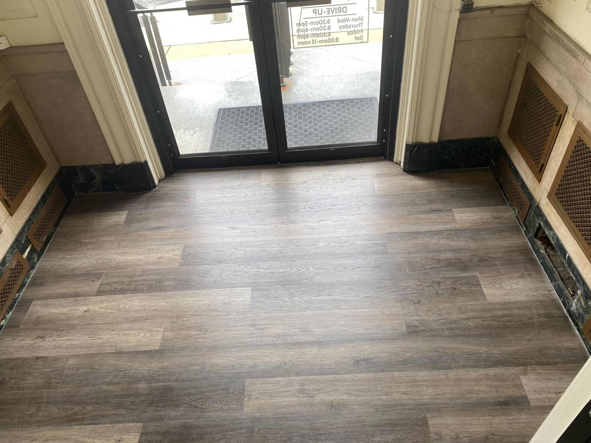 Empty hallway with wood-look flooring and glass entrance doors ahead
