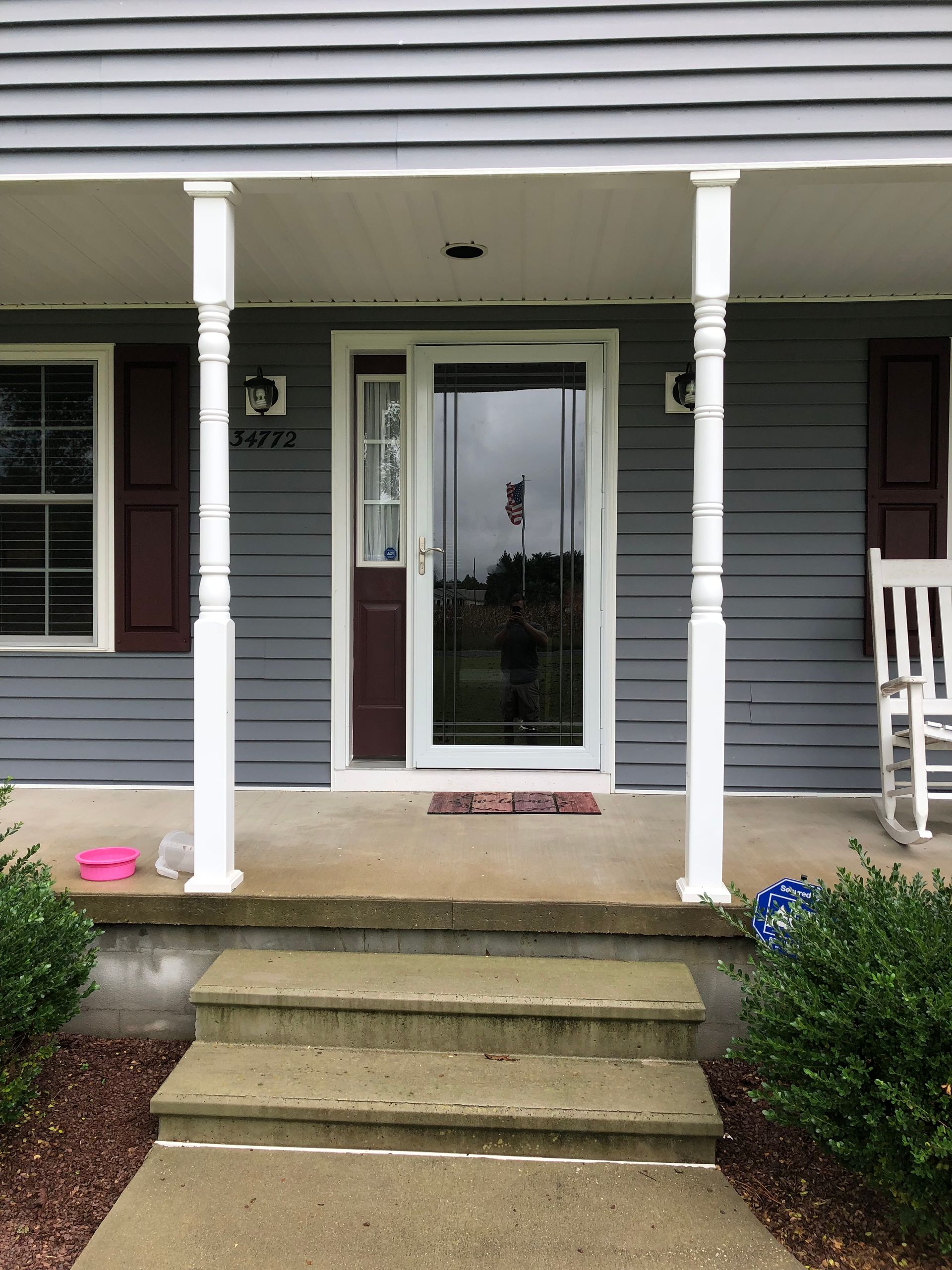 Front porch with white columns, gray siding, concrete steps, and a glass storm door.