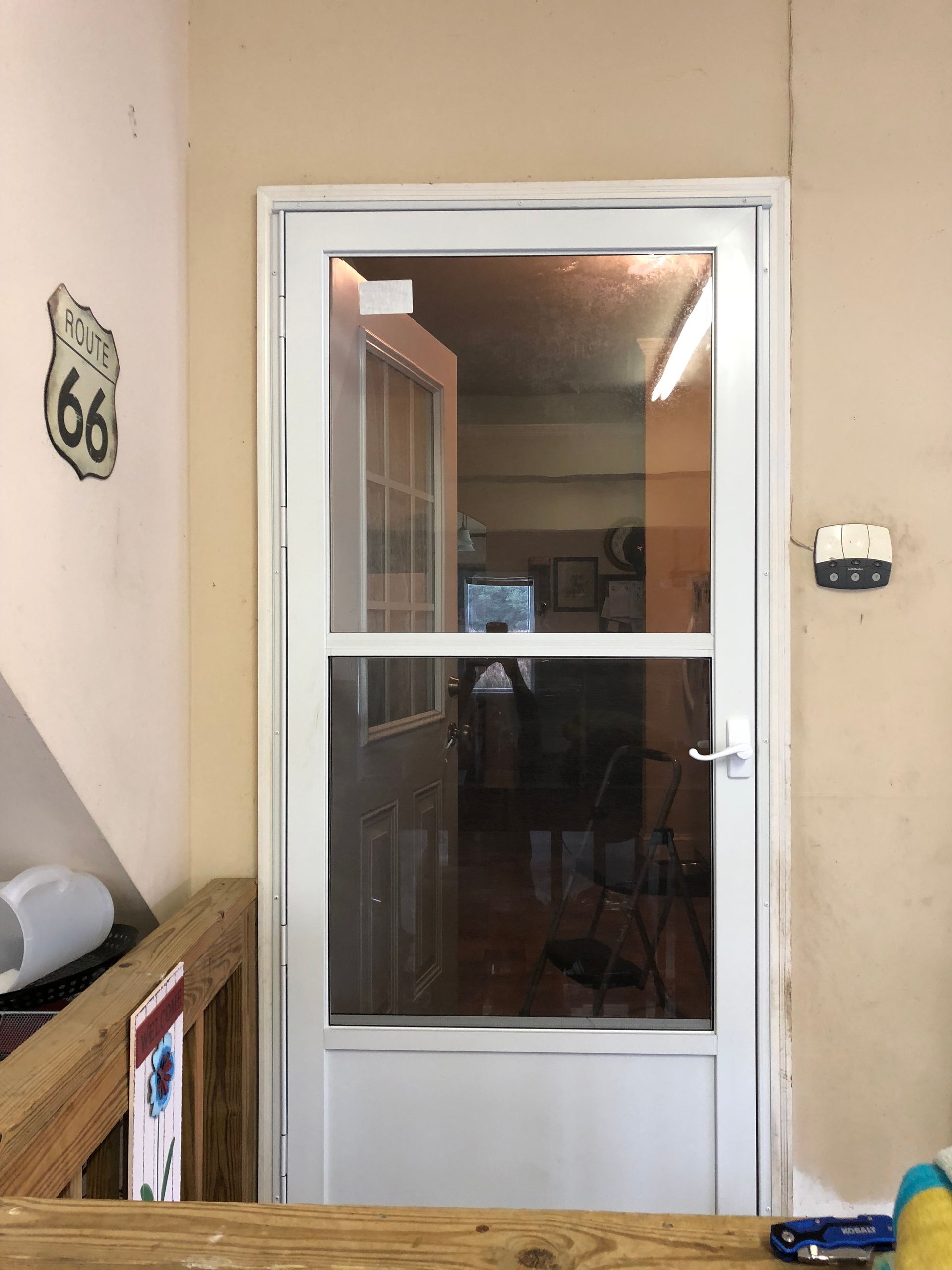 White storm door with glass panes in a hallway, framed by beige walls and a wooden bench.