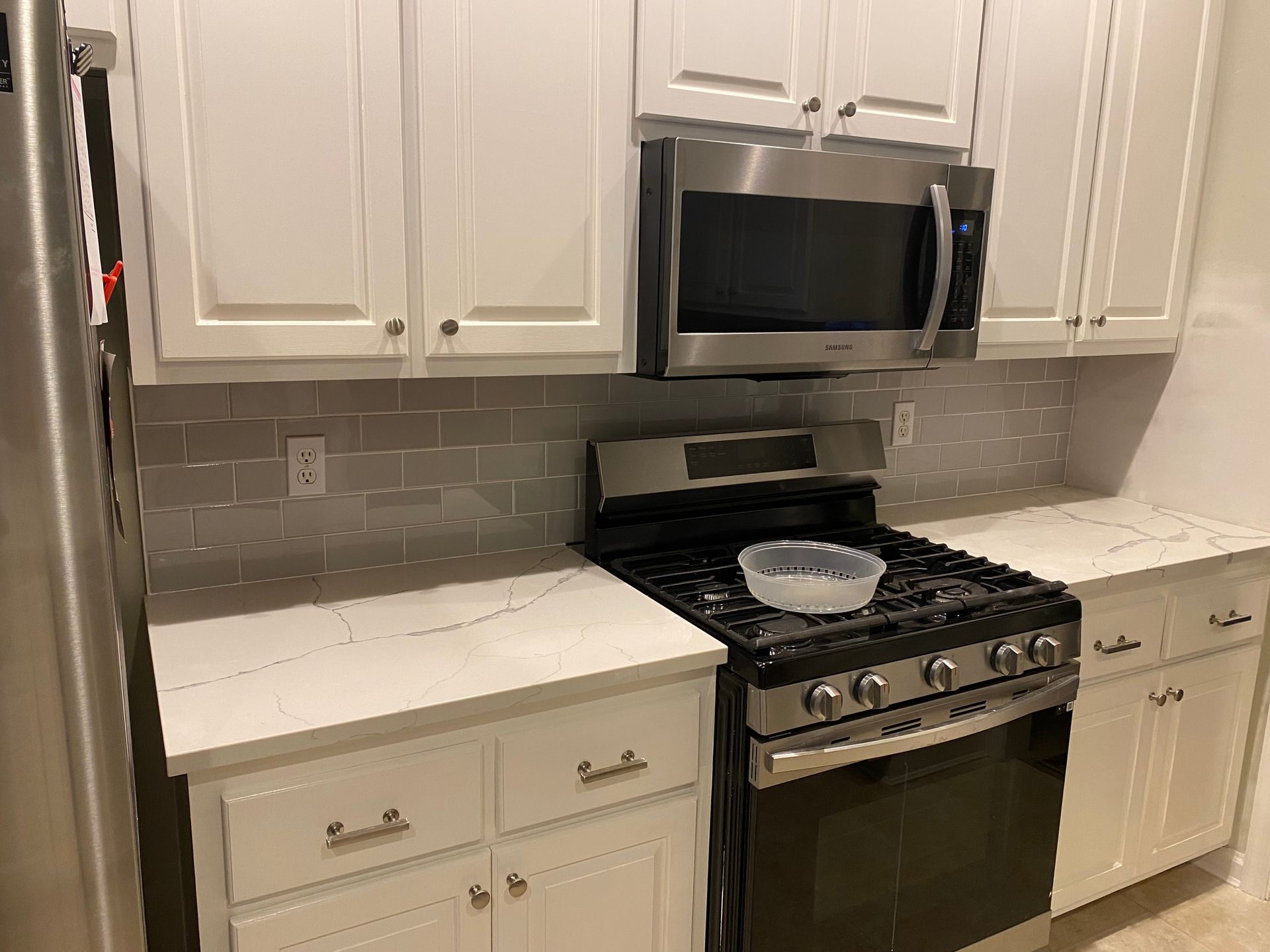 White kitchen with stainless steel stove, microwave, and cabinets, plus a tiled backsplash and countertop