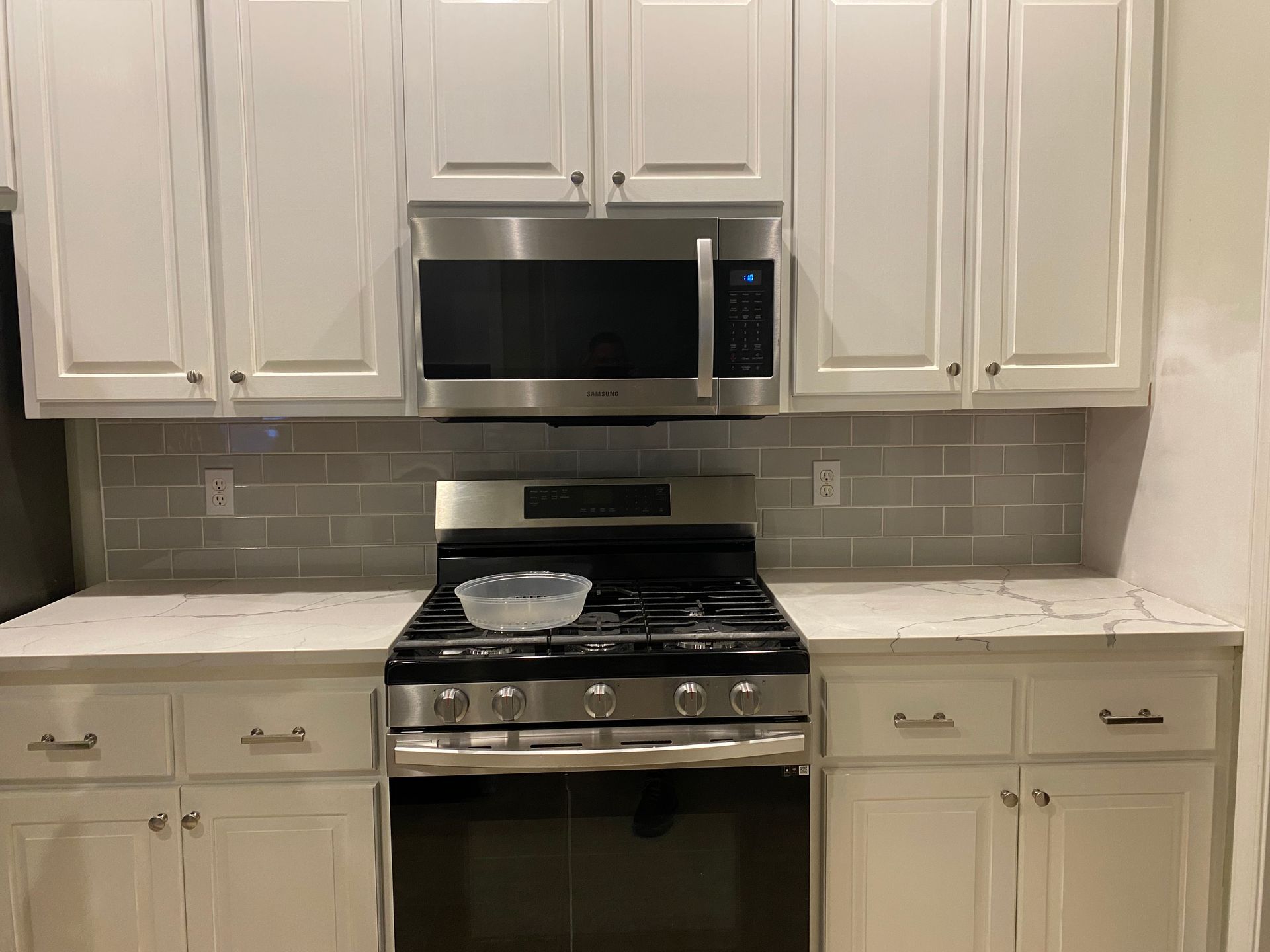 Modern kitchen with white cabinets, stainless steel appliances, and gray tile backsplash