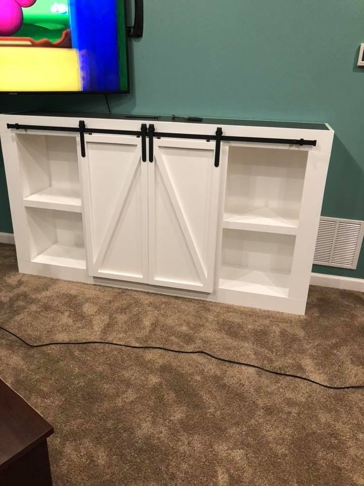 White barn-door style TV stand with shelves in a living room, beneath a wall-mounted TV