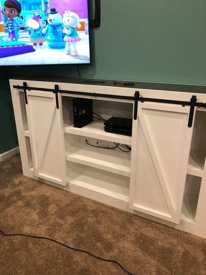 Living room TV wall with a white barn-door media console and visible electronics on shelves