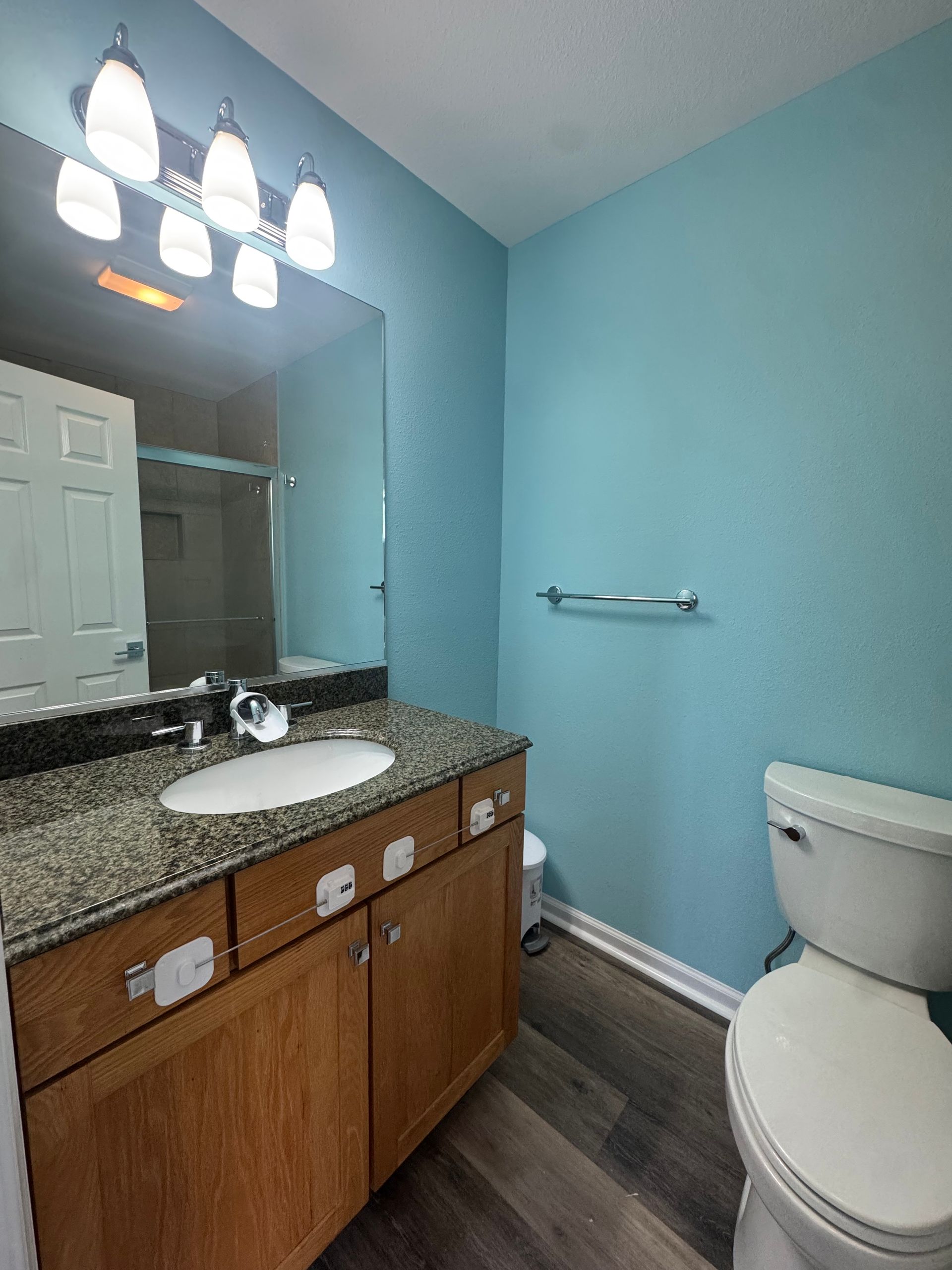 Bathroom with blue walls, wood vanity, mirror, sink, and toilet.