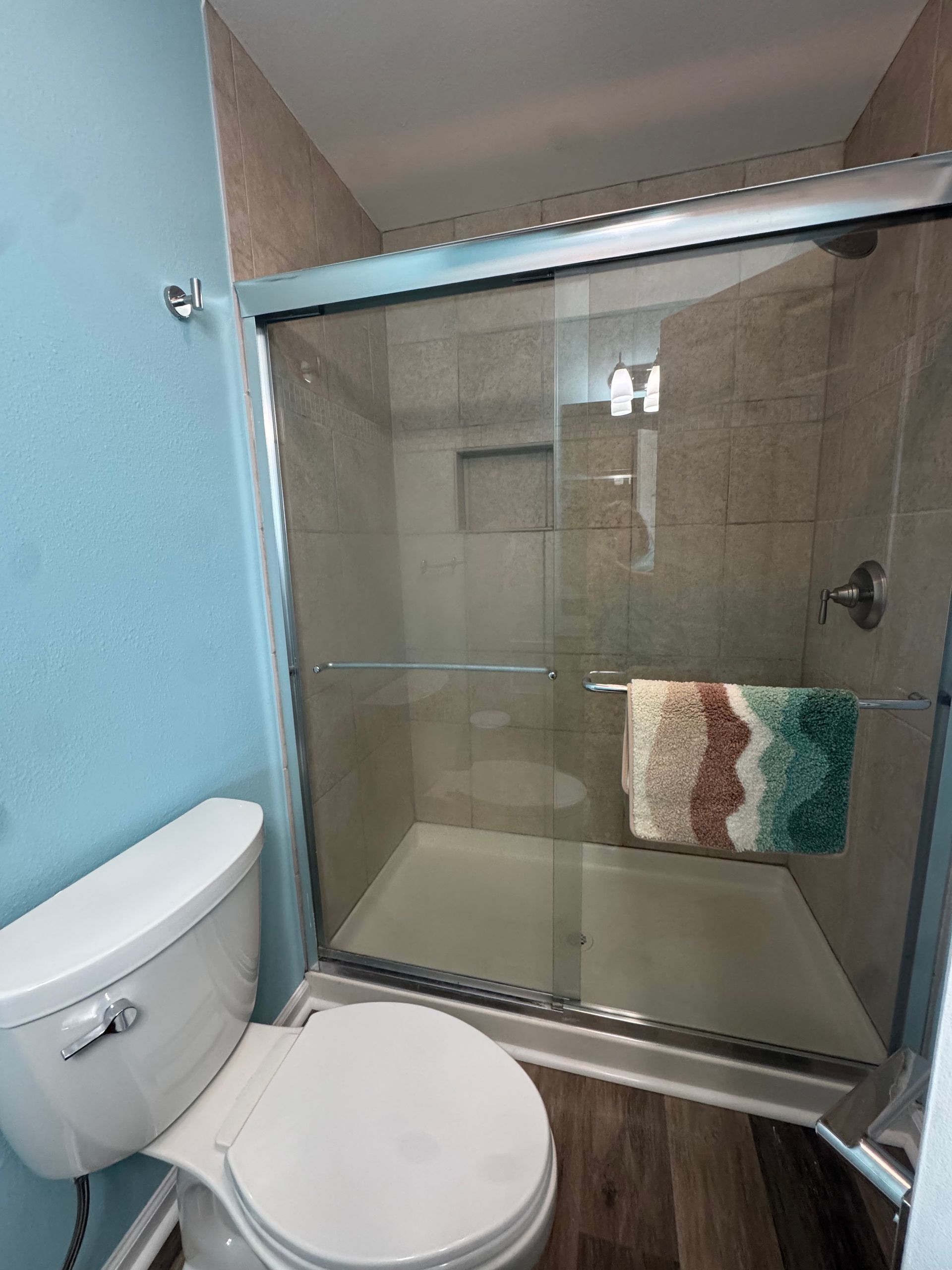 Small bathroom with toilet and glass-enclosed shower, beige tile walls, and striped towel hanging inside.