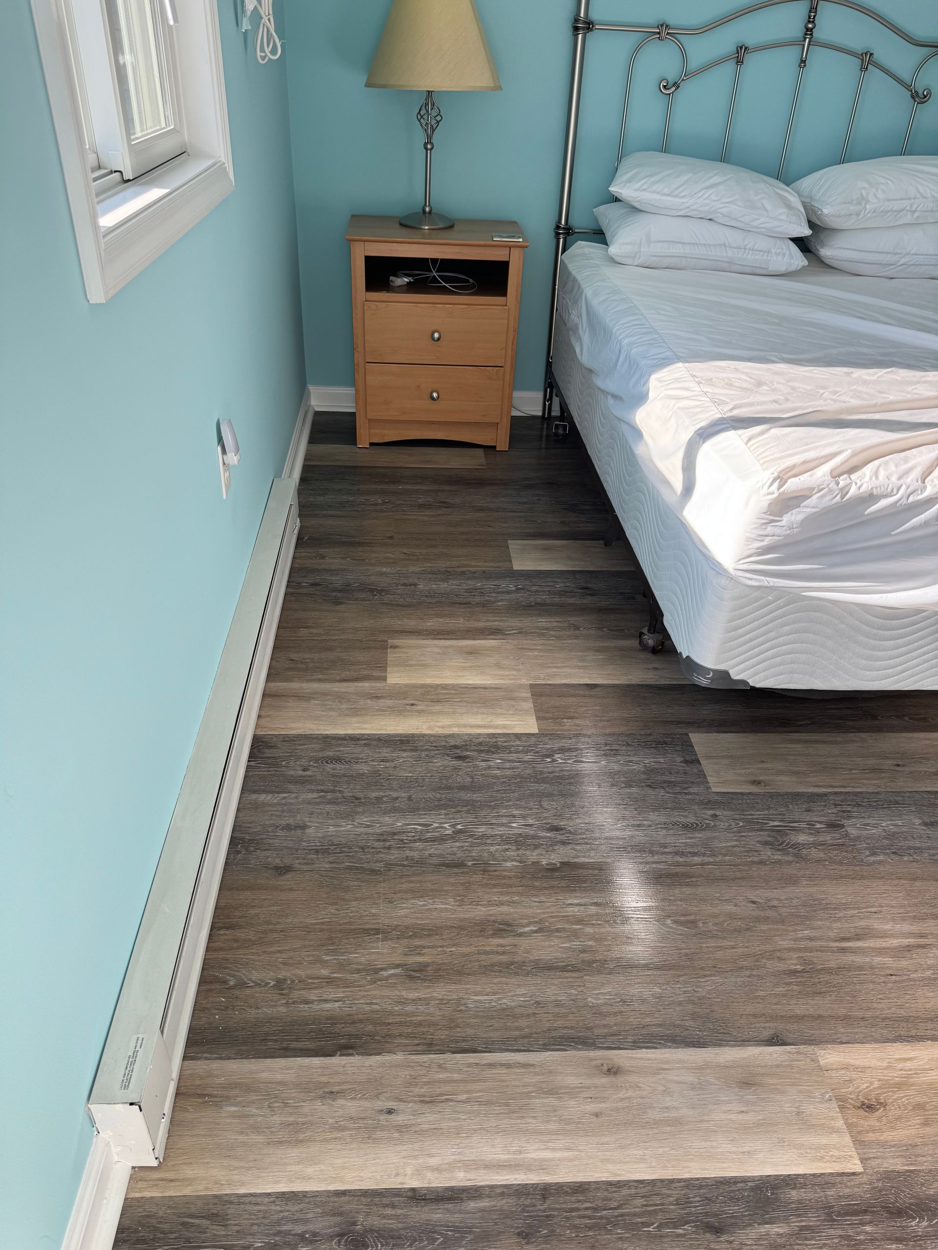 Narrow bedroom with blue walls, bed, nightstand, and wood-look flooring.