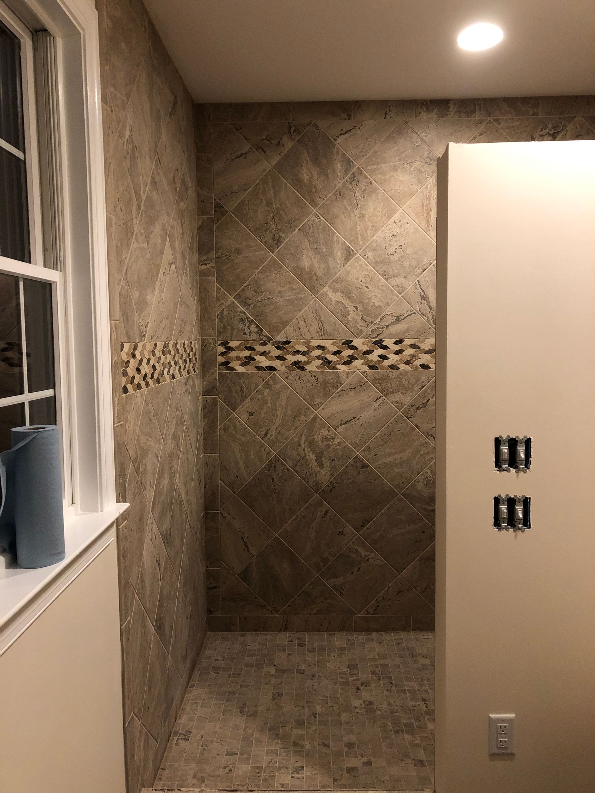 Bathroom shower alcove with brown tile, stone floor, and a white vanity edge on the left