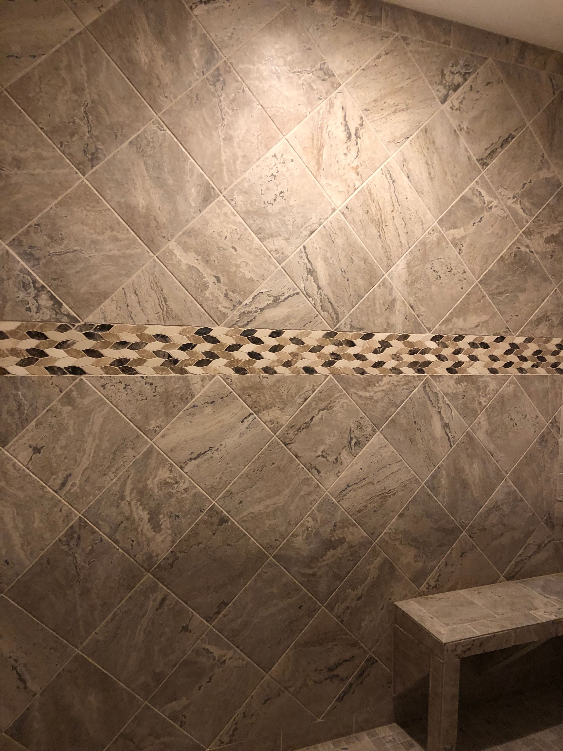Beige tiled shower wall with a decorative mosaic border and a small bench corner