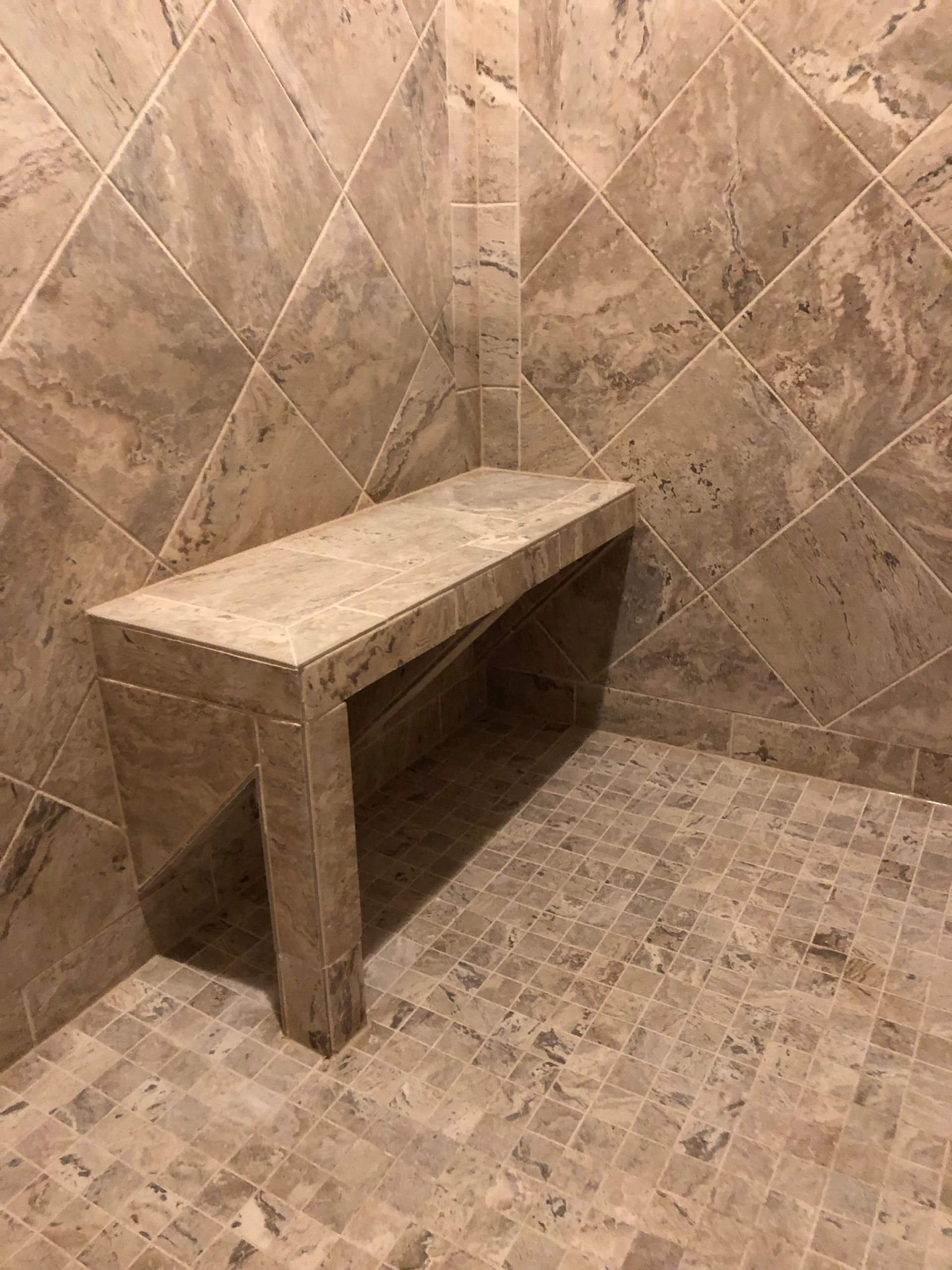 Stone bench in a tiled shower stall with beige walls and floor.