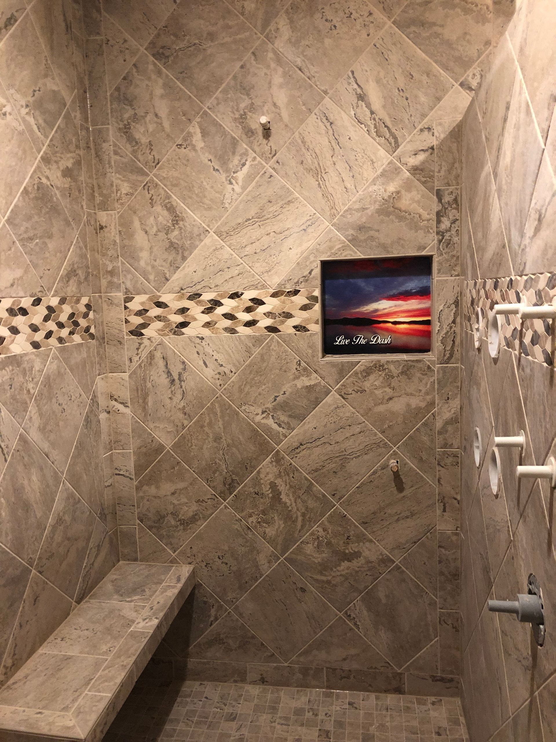 Stone-tiled shower with a mosaic border and a sunset picture on the wall