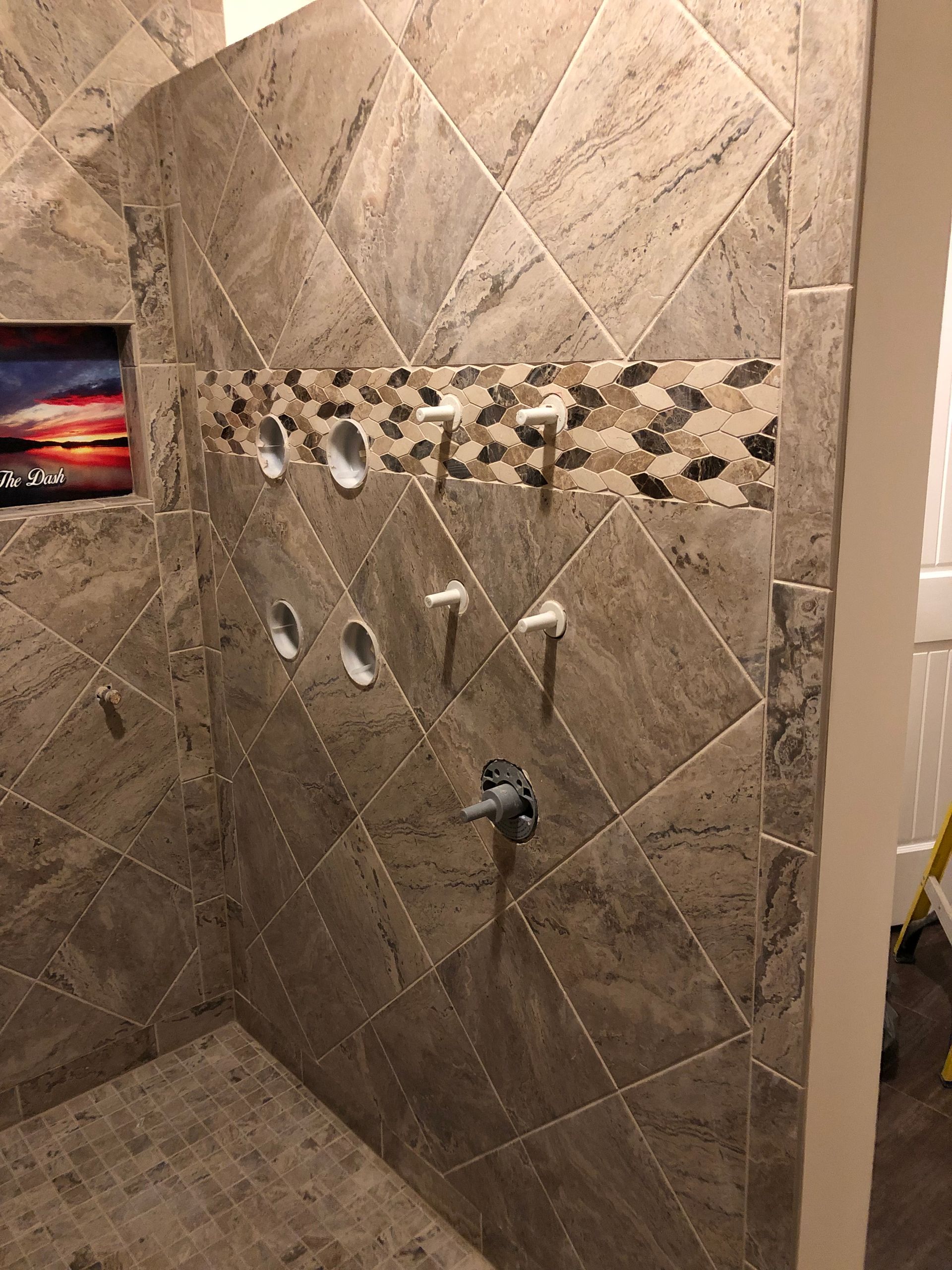 Empty tiled shower with multiple plumbing fixtures and checkerboard accent tiles