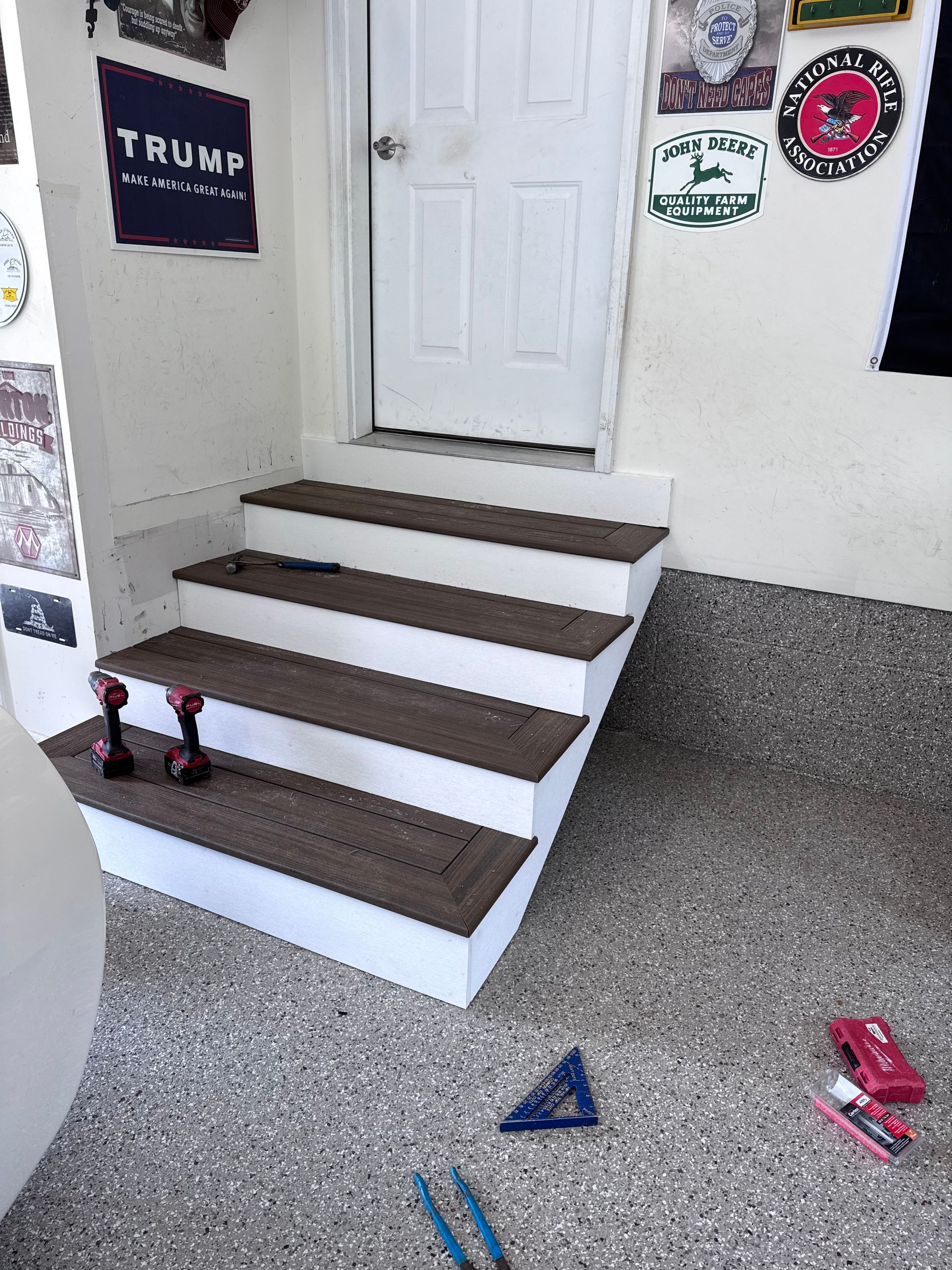 Front steps with white door, brown treads, and a speckled floor; small red and blue objects nearby