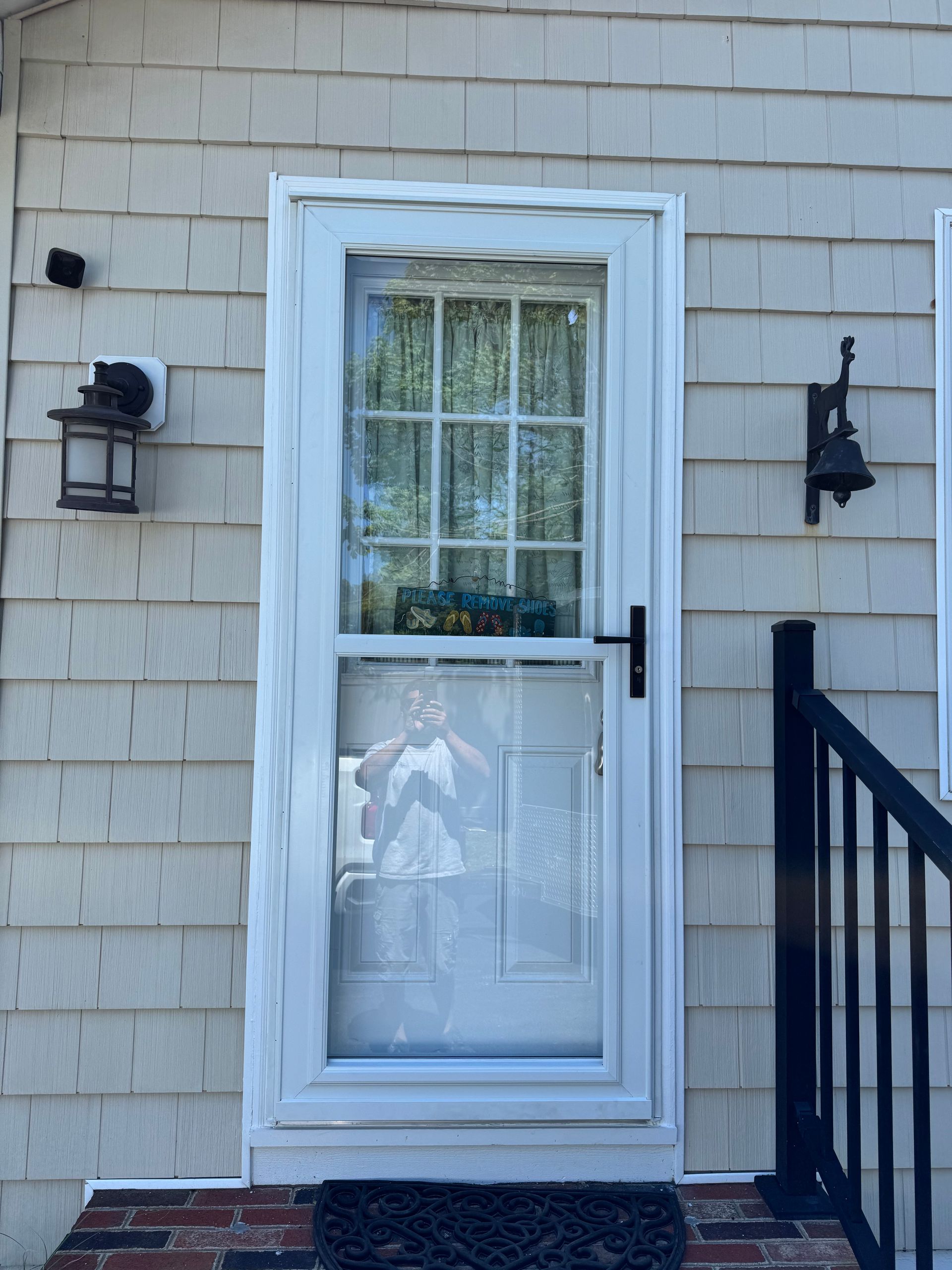 White front door with glass panel on beige siding, flanked by black lantern lights and a railing.