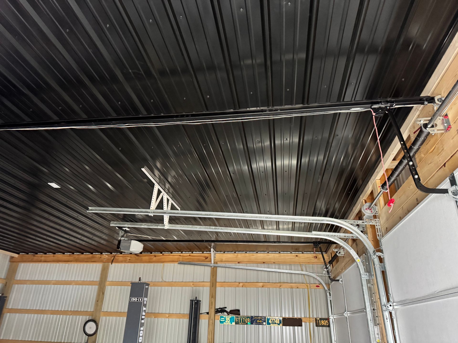 Industrial ceiling with exposed black corrugated metal, white pipes, and conduit in a workshop or garage