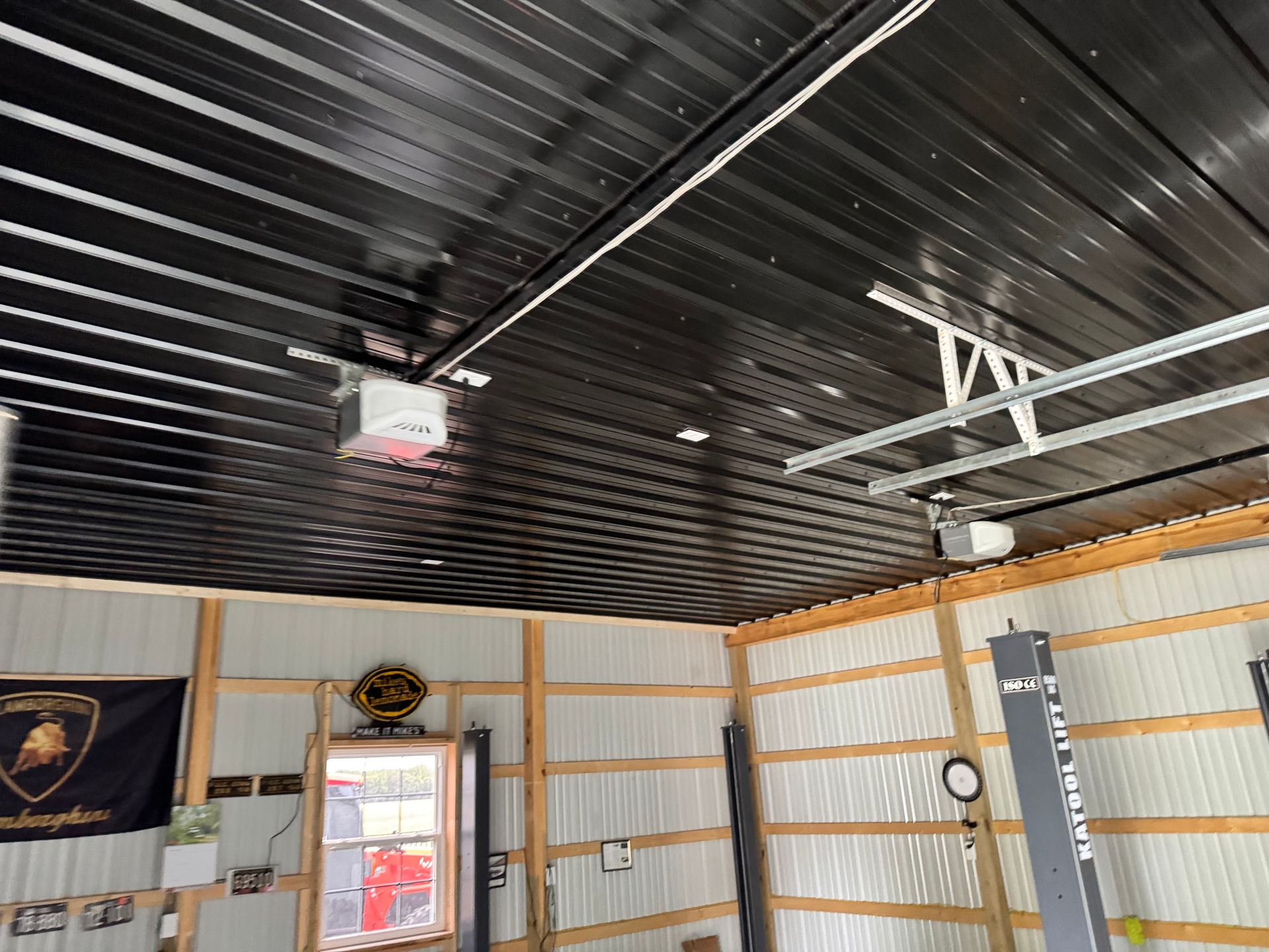 Industrial workshop interior with black metal ceiling, white walls, and wall-mounted fan and clock