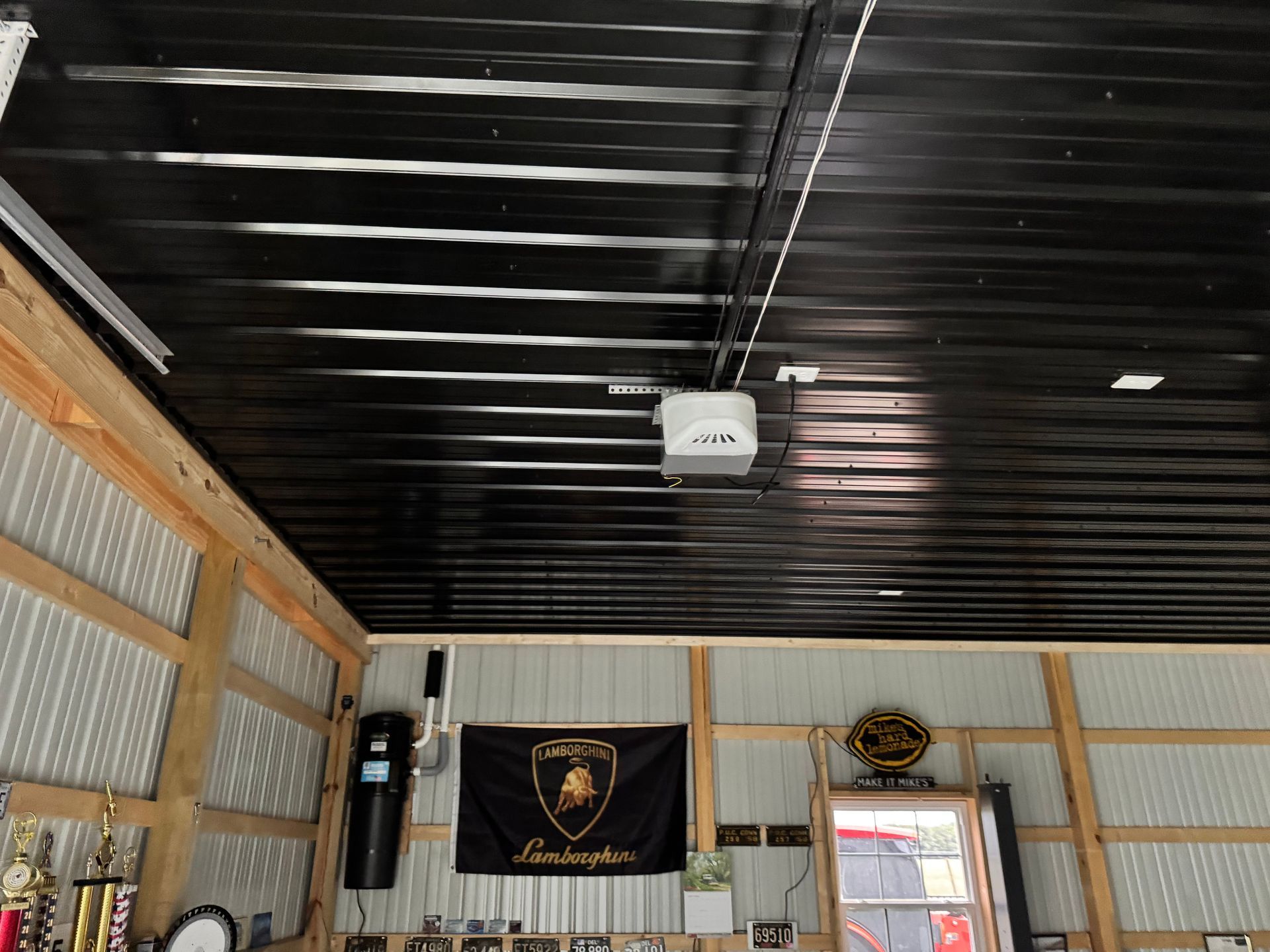 Interior of a garage with a black ceiling, exposed beams, wall banners, and an open doorway with daylight