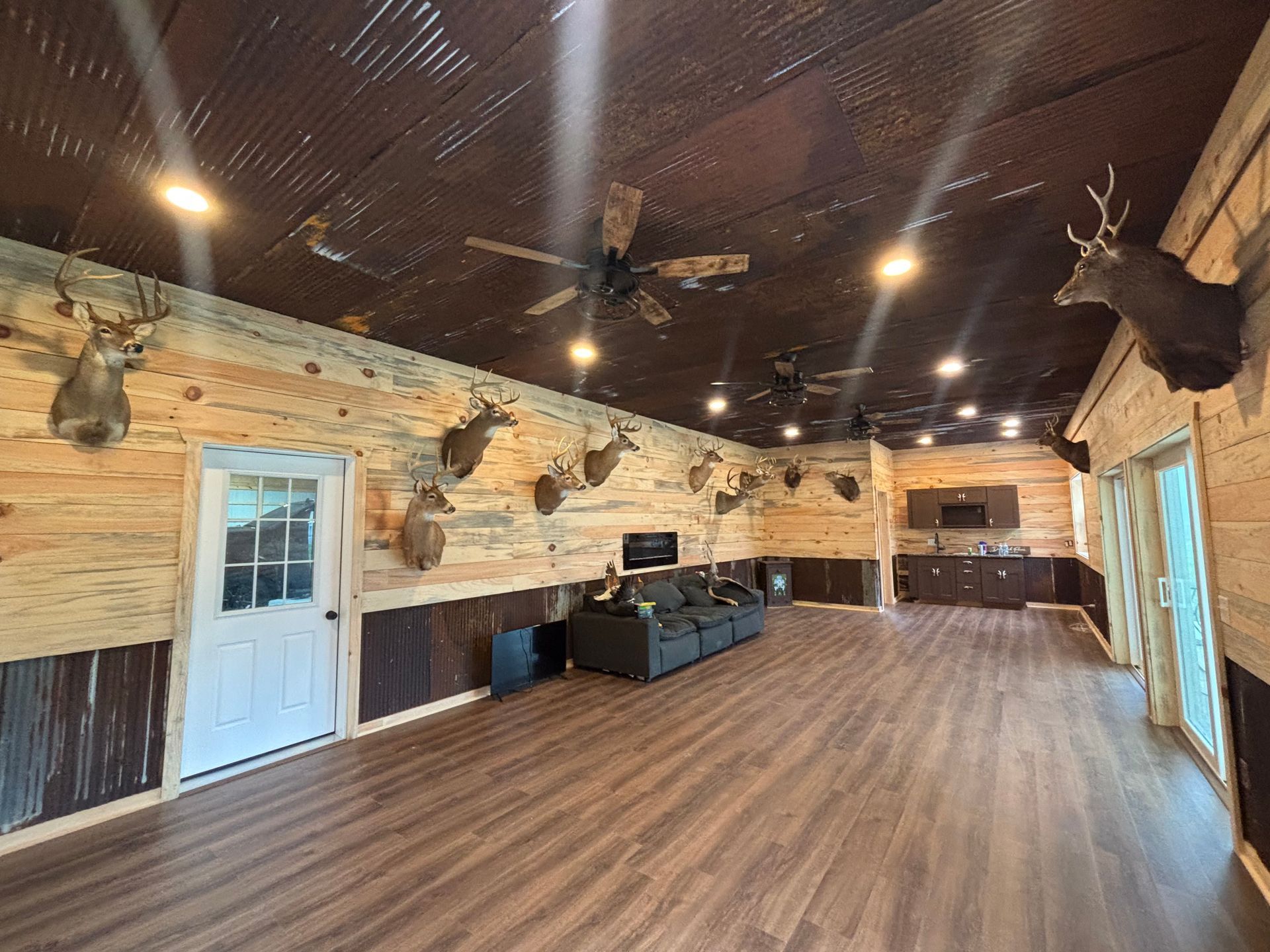 Spacious rustic lodge interior with wood walls, mounted deer heads, and a wooden floor.