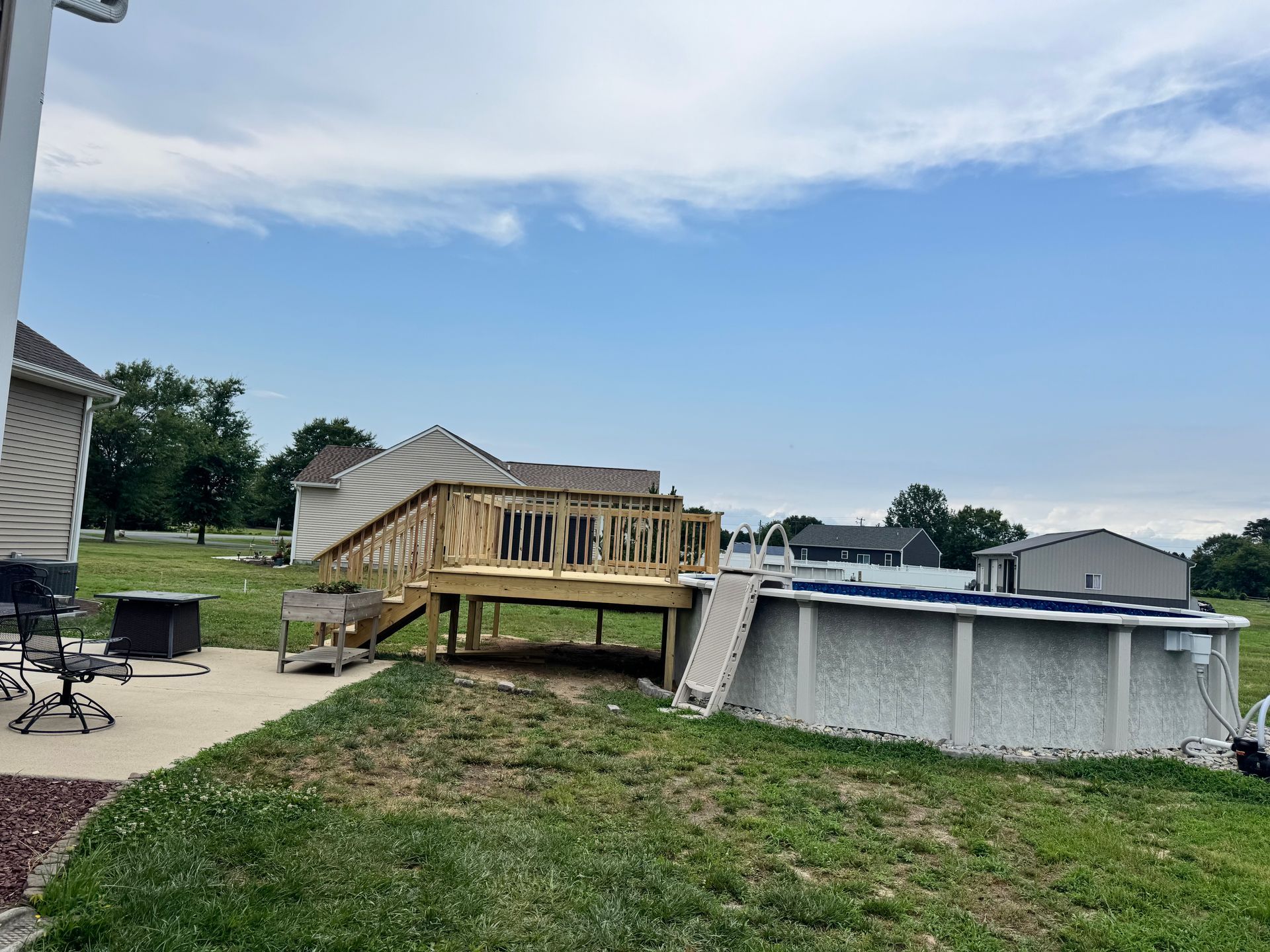 Backyard with a raised wooden deck under construction beside an above-ground pool on a grassy lot